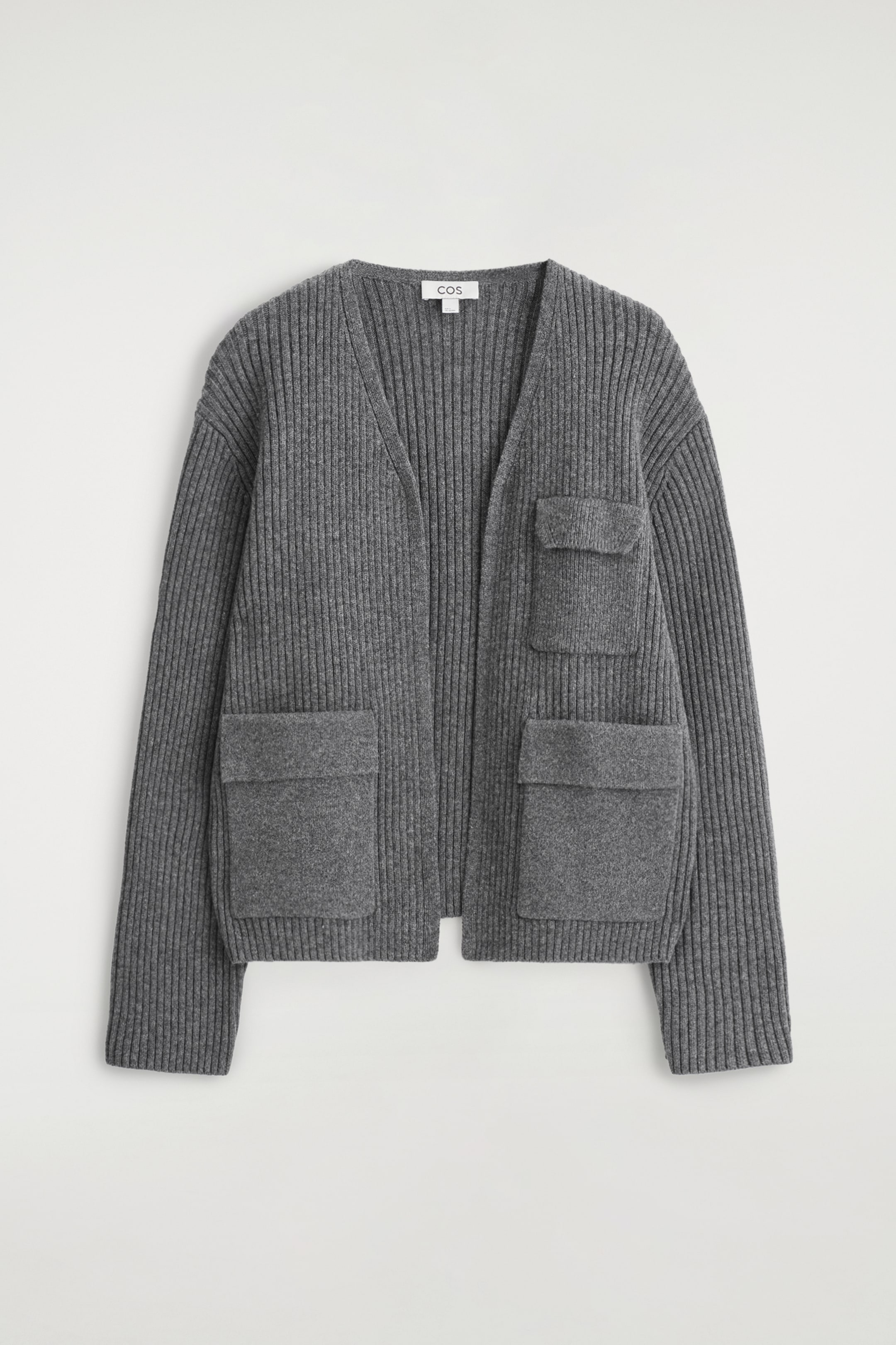 Visualizza immagine più grande: Un cardigan a maglia grigia, grossa e a coste viene presentato dalla parte anteriore. Presenta uno scollo a V aperto, maniche lunghe e tre tasche con patta: una tasca superiore più piccola e due tasche inferiori più grandi.