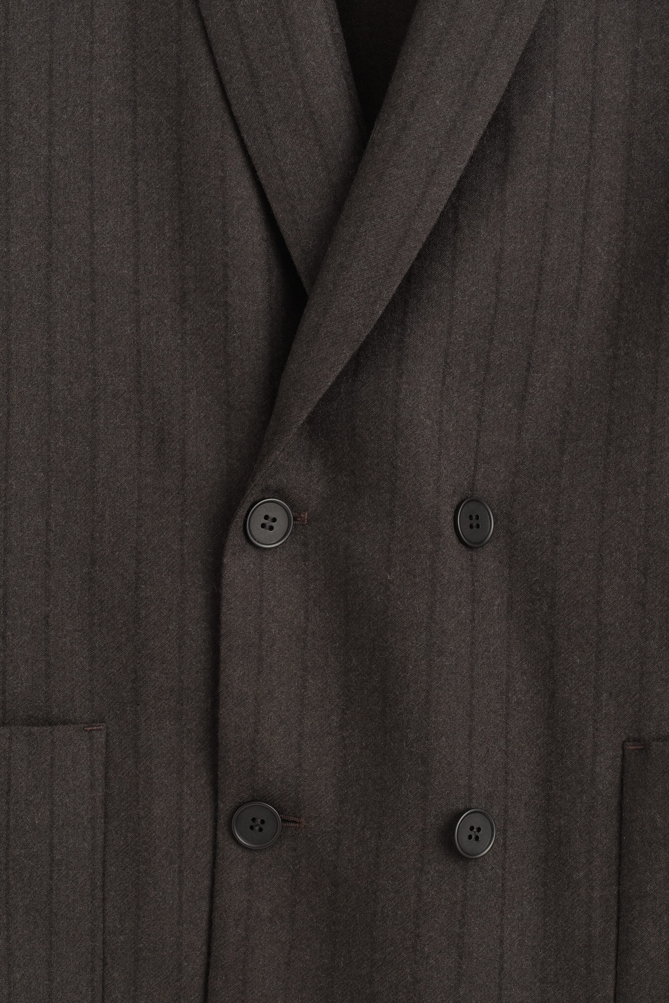A dark brown pinstriped wool blazer is shown in a close-up front view, featuring a double-breasted closure with four black buttons and overlapping lapels. The image highlights the tactile twill texture and subtle vertical pinstripes of the fabric. A dark brown pinstriped wool blazer is shown in a close-up front view, featuring a double-breasted closure with four black buttons and overlapping lapels. The image highlights the tactile twill texture and subtle vertical pinstripes of the fabric.