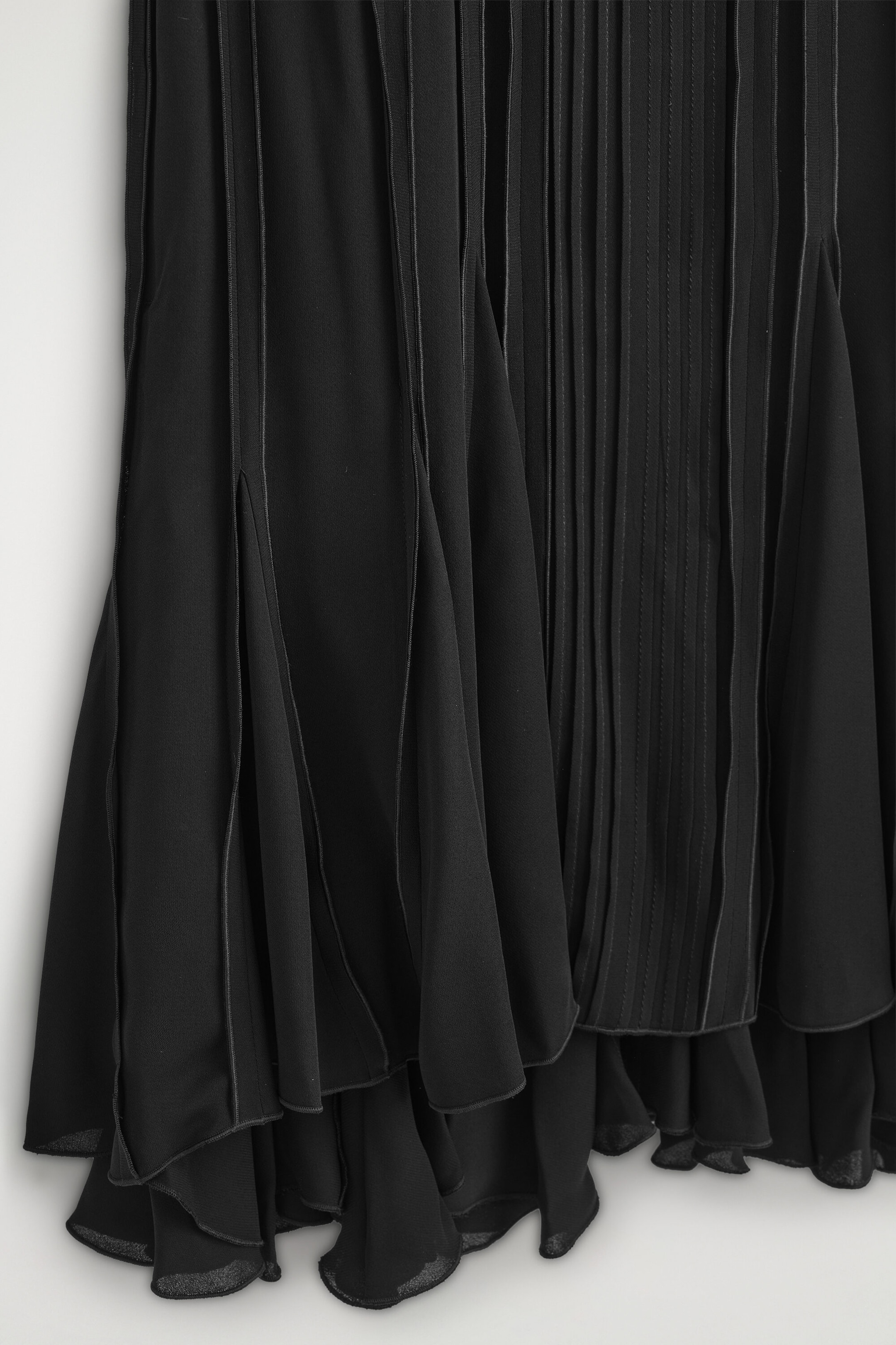 The voluminous pleated midi dress showcases its intricate vertical pleating with fine piped detailing in a close-up front view. The dress features a tiered, fluid hemline with voluminous ruffled layers that drape softly. The voluminous pleated midi dress showcases its intricate vertical pleating with fine piped detailing in a close-up front view. The dress features a tiered, fluid hemline with voluminous ruffled layers that drape softly.