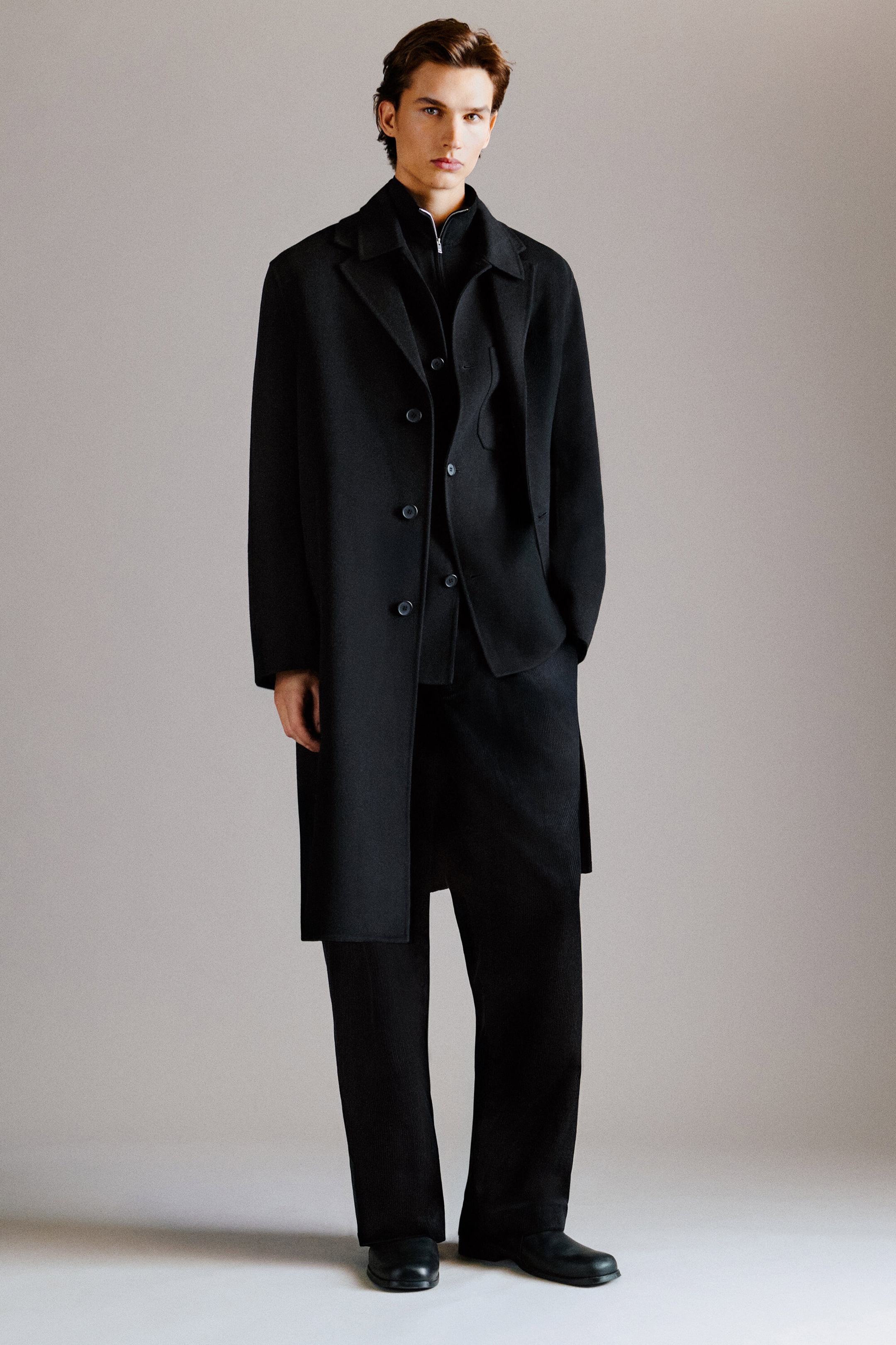 The black Tailored Double-Faced Wool-Blend Coat is worn front-facing, highlighting its structured, mid-length silhouette, notch lapels, and button detailing. It is styled over a black layered jacket and paired with the black Pleated Relaxed-Fit Tapered Corduroy Pants, which drape in a loose, relaxed fit. The black Tailored Double-Faced Wool-Blend Coat is worn front-facing, highlighting its structured, mid-length silhouette, notch lapels, and button detailing. It is styled over a black layered jacket and paired with the black Pleated Relaxed-Fit Tapered Corduroy Pants, which drape in a loose, relaxed fit.