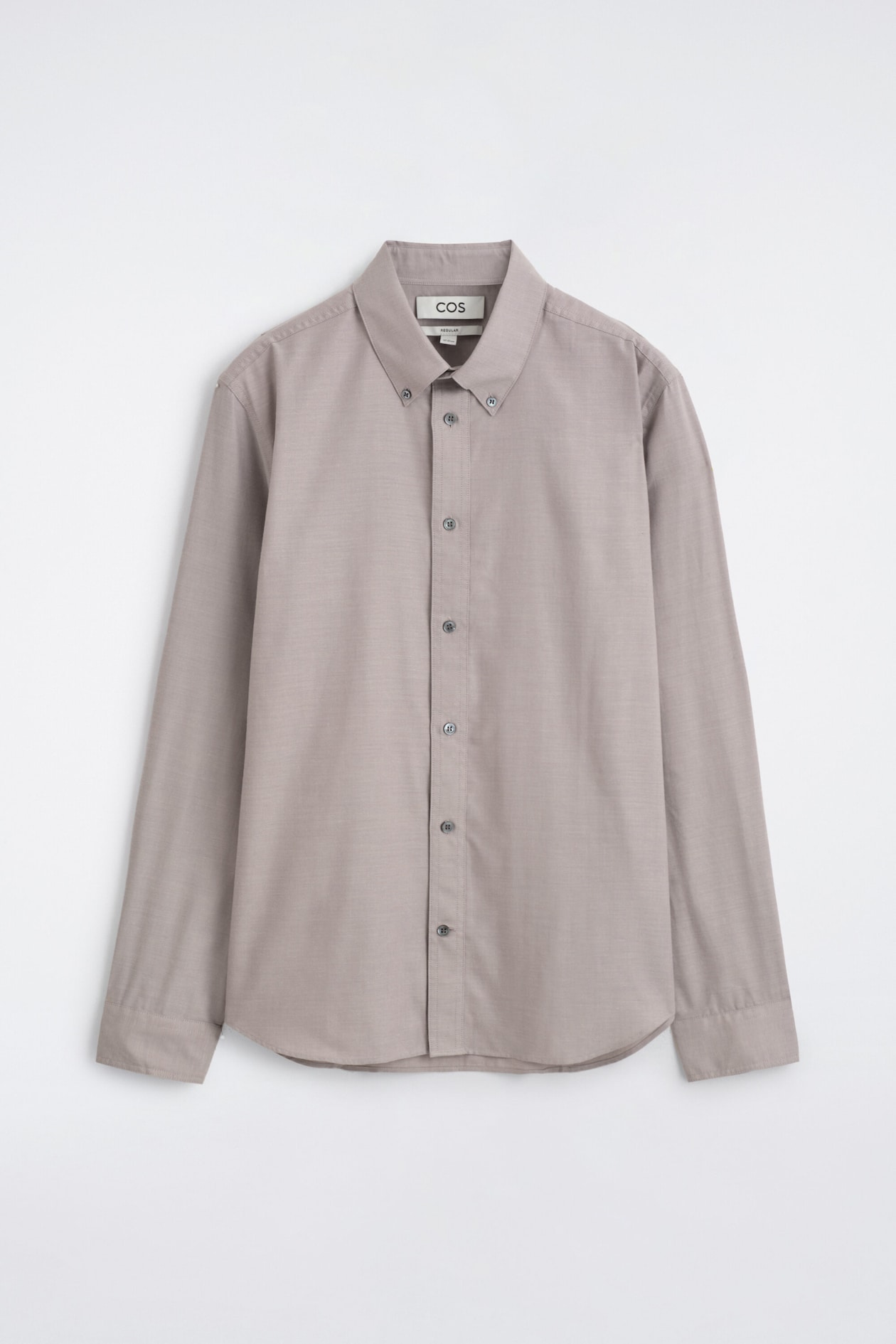 A button-down collar brushed oxford shirt in a muted taupe colour is hanging in a front-facing view, showcasing its clean structure and regular fit. The shirt features a classic button-down collar, a central button-up placket, long sleeves with buttoned cuffs, and a subtly curved hem.