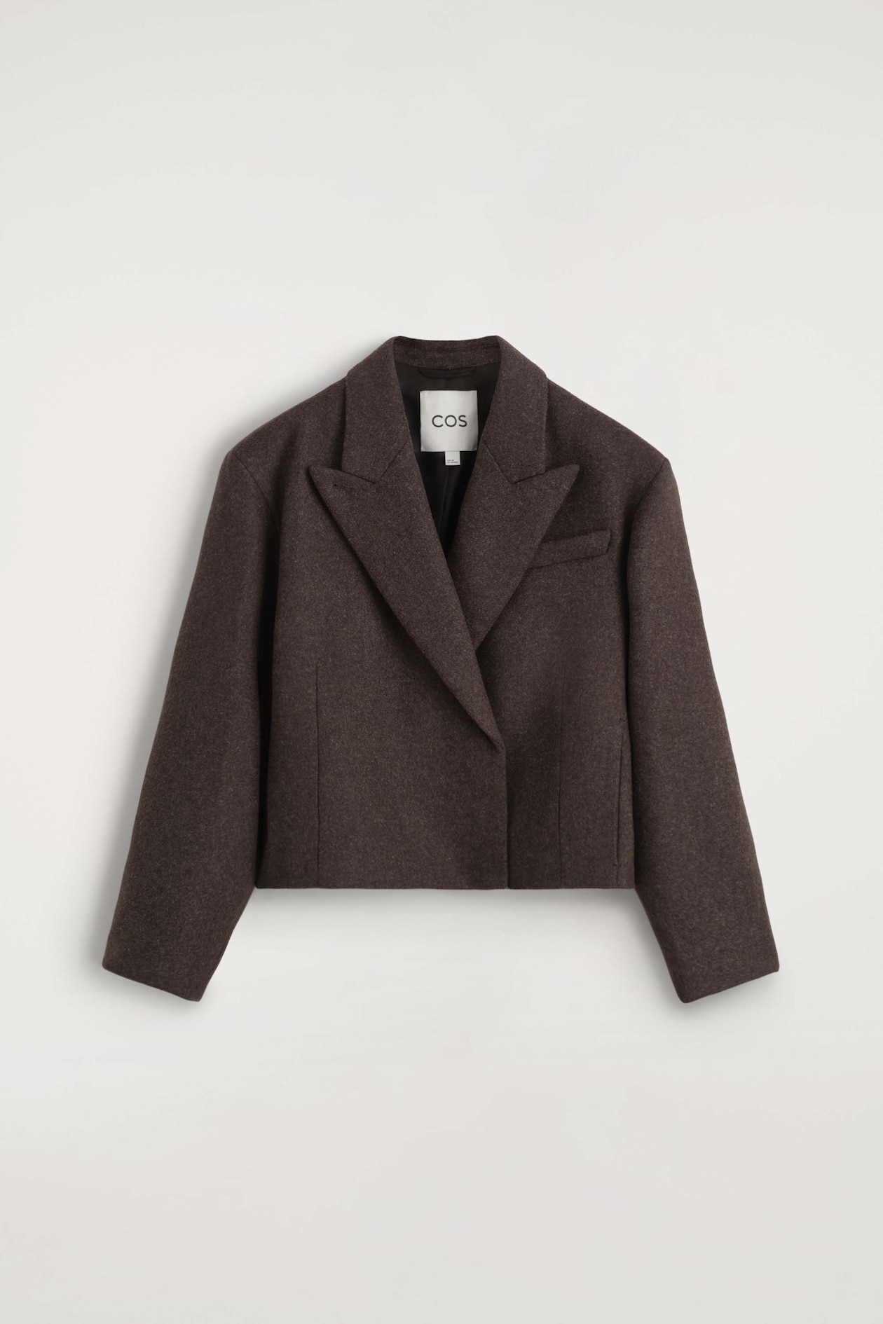 The oversized cropped boiled wool-blend blazer is shown from the front, showcasing its boxy, cropped silhouette in a textured dark brown fabric. It features wide peak lapels, long relaxed sleeves, and a single chest welt pocket.