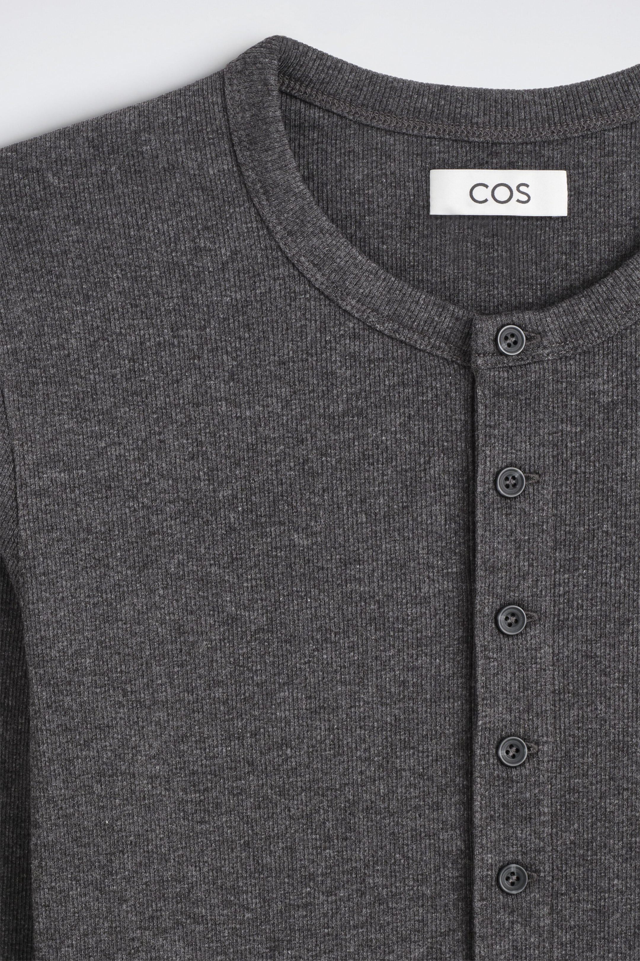 The slim ribbed cotton long-sleeved Henley T-shirt is shown in a close-up front view, highlighting its dark grey ribbed-knit fabric and crew neckline. The design features a vertical Henley placket with five dark buttons.