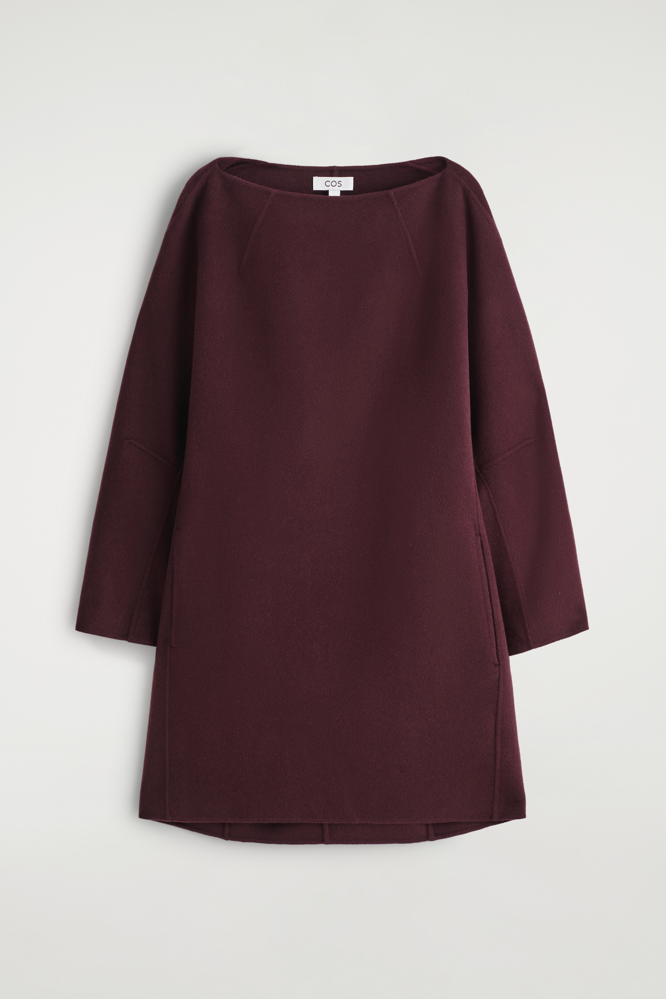 Agrandir l'image: L'avant de la ROBE MINI EN LAINE DOUBLE FACE est présenté dans une couleur bordeaux profond. Elle présente un col bateau, des manches longues raglan avec un détail de couture horizontale au bas de la manche, et des poches verticales dans la couture. Une étiquette blanche 'COS' est visible à l'arrière du cou.