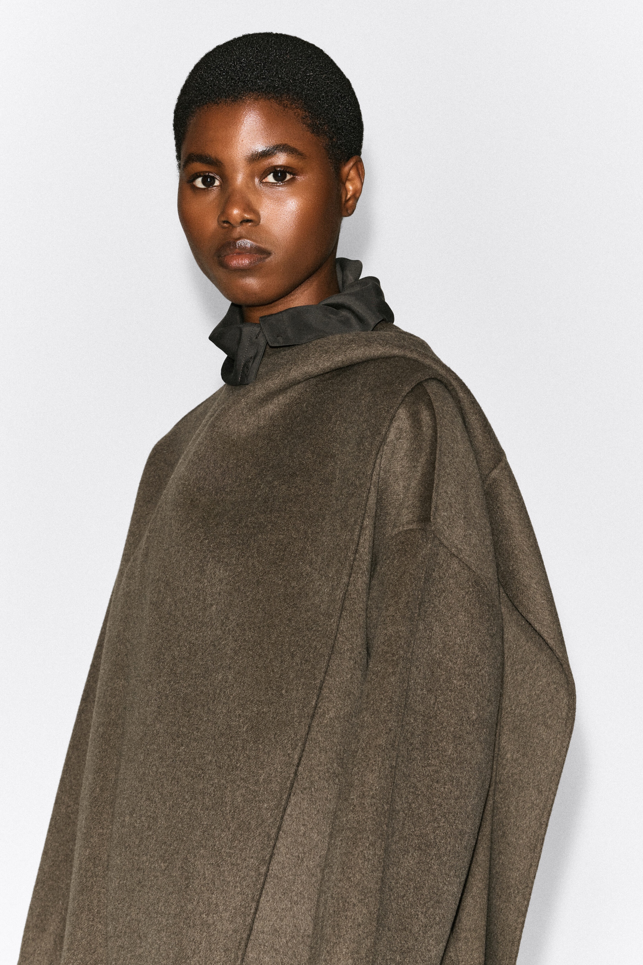 A double-faced wool-blend scarf jacket in textured brown is being worn by the model, featuring a draped scarf detail that wraps over the shoulder. The jacket is layered over a dark grey, high-collared shirt visible at the neck. A double-faced wool-blend scarf jacket in textured brown is being worn by the model, featuring a draped scarf detail that wraps over the shoulder. The jacket is layered over a dark grey, high-collared shirt visible at the neck.