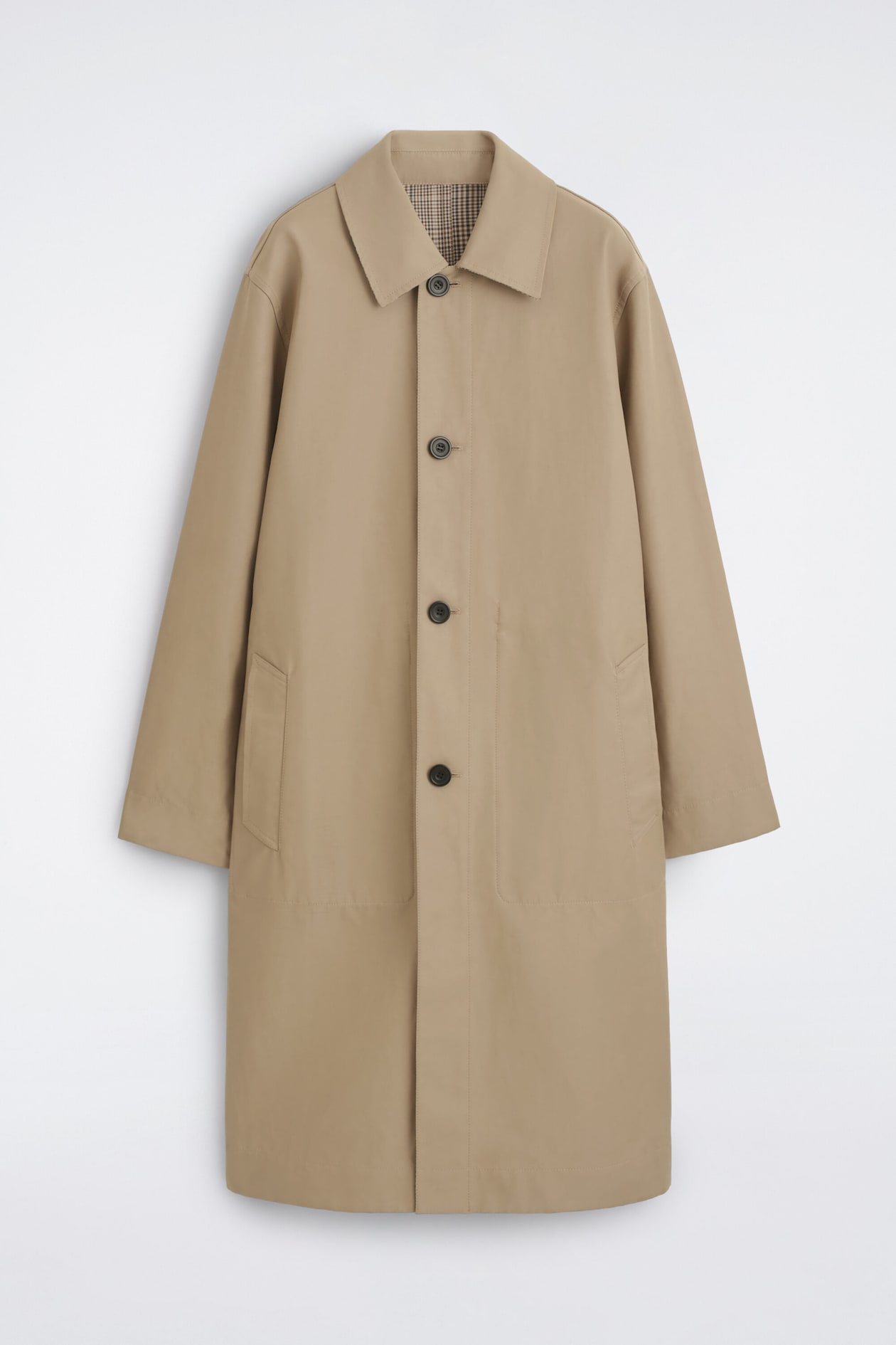 Le manteau de voiture réversible à carreaux est présenté de face, avec un extérieur uni beige, un col classique, une fermeture boutonnée et deux poches passepoilées latérales. Un motif à carreaux brun et beige apparaît au niveau du col intérieur, mettant en valeur la conception réversible du manteau.