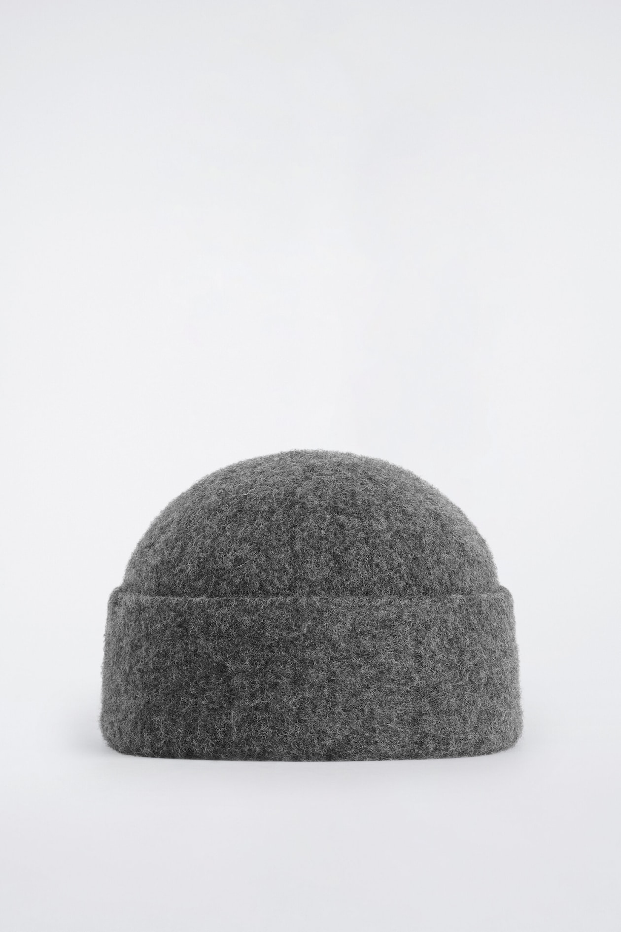 Un bonnet gris foncé est présenté de face, montrant une calotte arrondie et un large revers replié. Le bonnet présente une apparence très texturée, duveteuse et de style feutré.