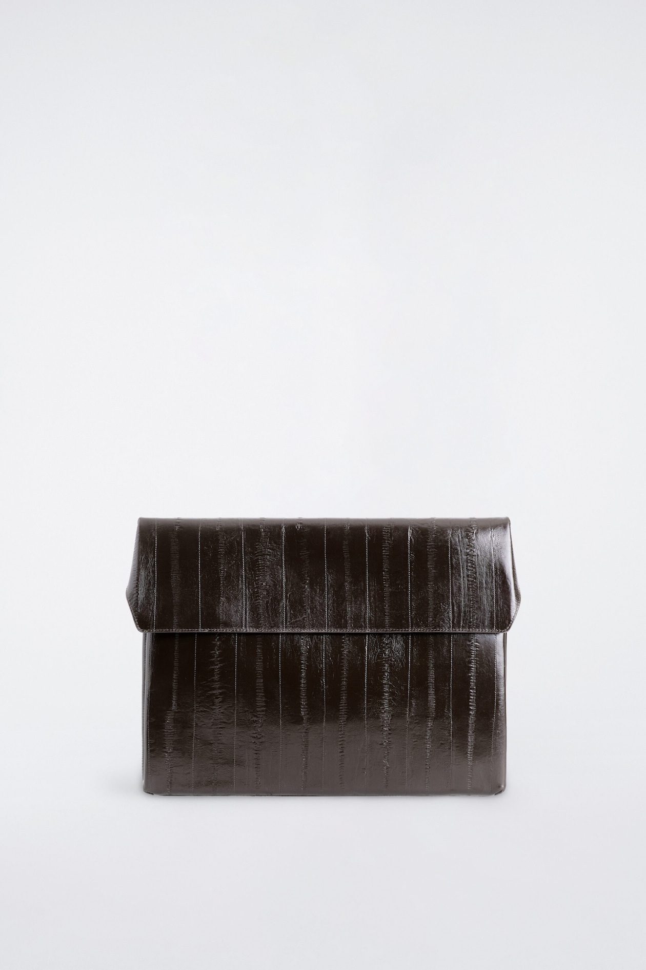 Die ENVELOPE LAPTOP SLEEVE – LEATHER ist in einer Frontansicht dargestellt und zeigt eine dunkelbraune, glänzende Lederkonstruktion mit vertikaler Paneel-Detailierung. Sie verfügt über eine strukturierte, rechteckige Form mit einem umklappbaren Umschlagverschluss.