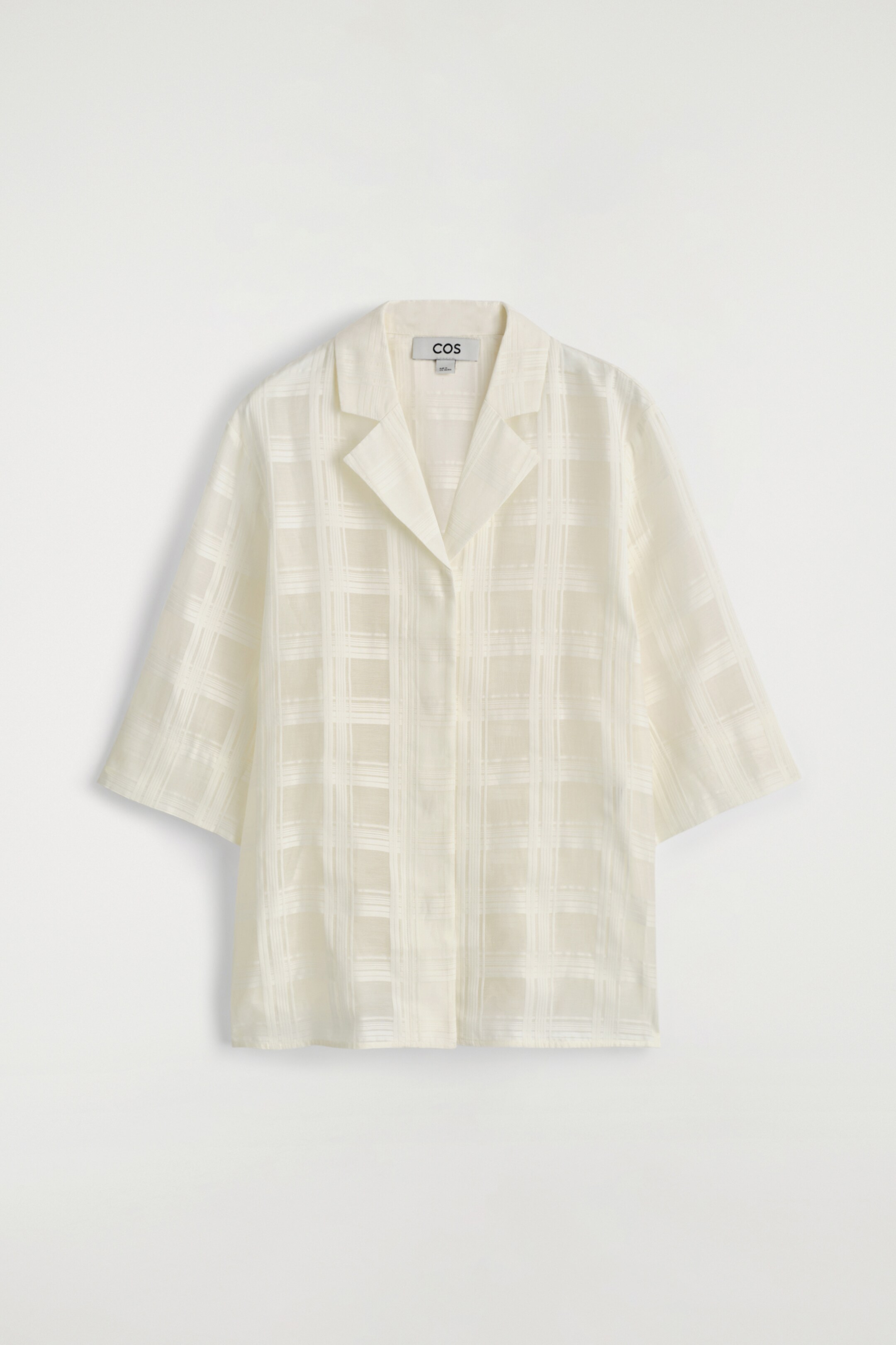 Ver imagen más grande: Una camisa de color crema, semi-transparente, se presenta desde el frente, con un motivo de cuadros tejidos, un cuello resort abierto y mangas de tres cuartos de largo. Muestra un ajuste relajado con una tapeta frontal oculta.