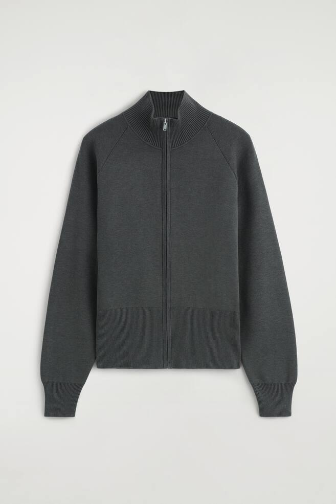 La chaqueta de punto con cuello chimenea y cremallera se muestra de frente, con un tejido de punto fino gris oscuro, un cuello alto acanalado y una cremallera frontal de longitud completa. La prenda presenta mangas raglÃ¡n con puÃ±os largos acanalados y un bajo ancho acanalado. - 1