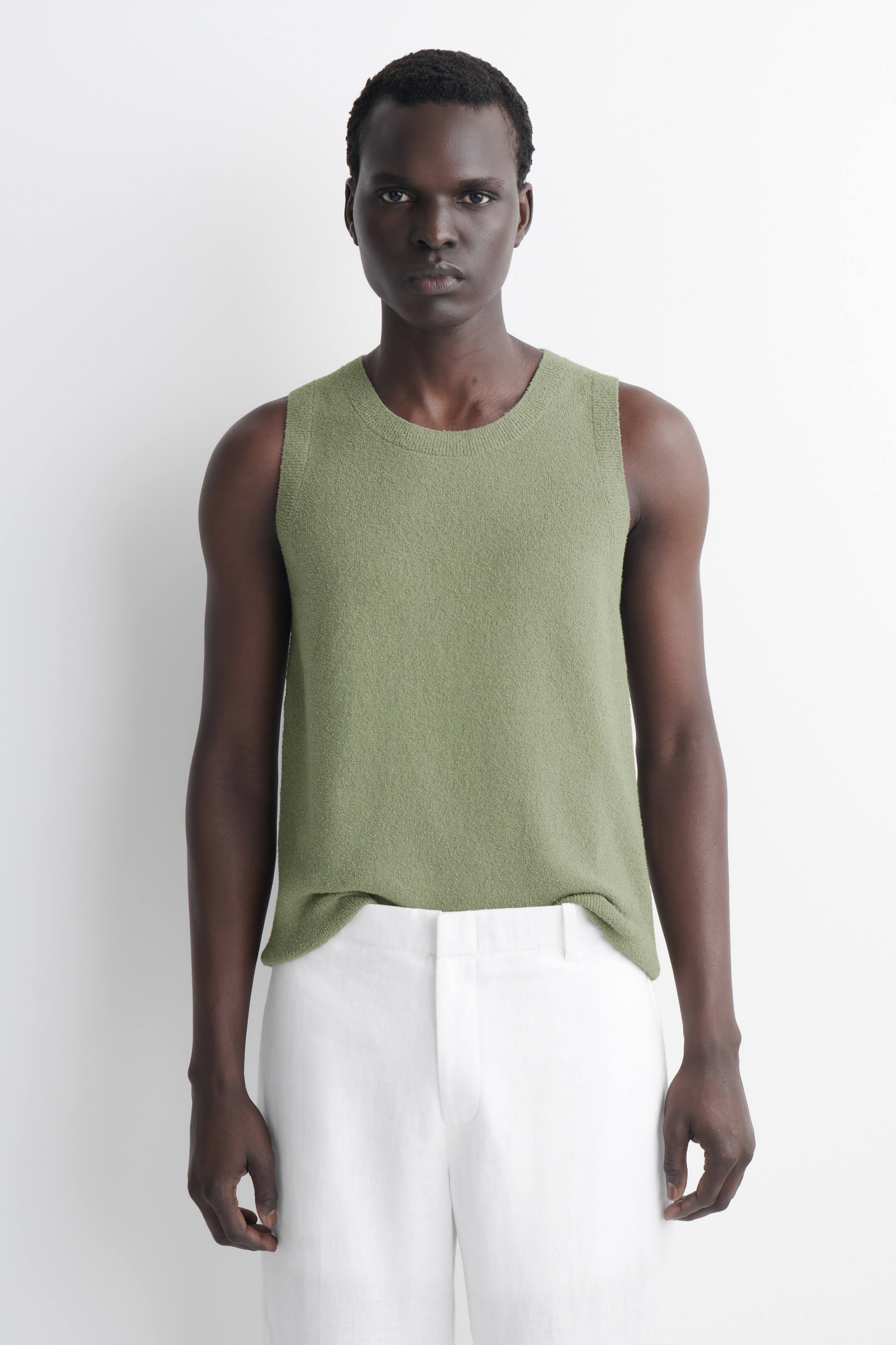 Visualizza l'immagine ingrandita: Un top senza maniche in maglia verde oliva viene presentato, caratterizzato da un girocollo, giromanica rifiniti e una superficie strutturata. Presenta una vestibilità rilassata, con l'orlo che si appoggia liberamente alla vita.