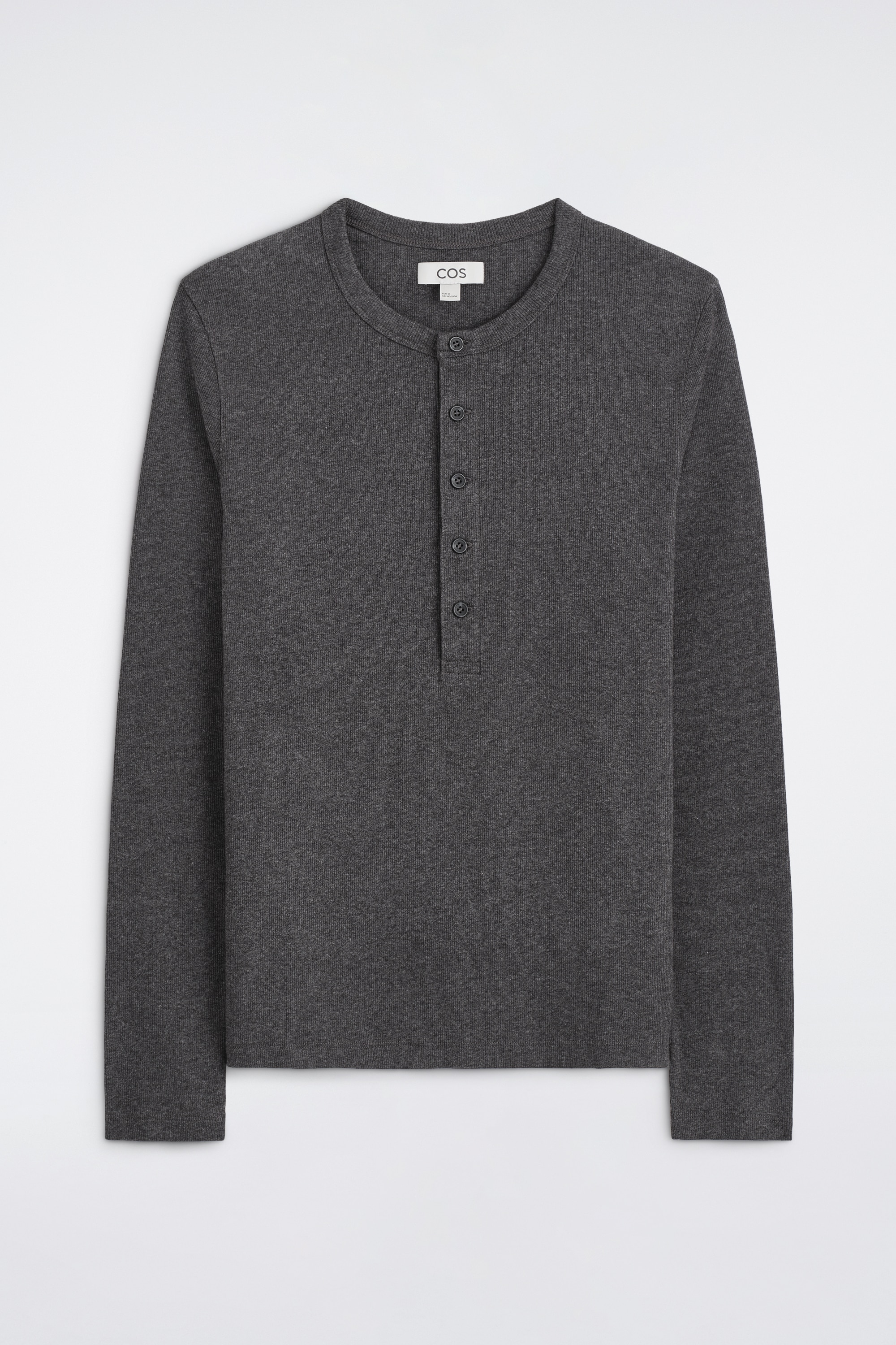 Het slim fit, geribde katoenen henley T-shirt met lange mouwen wordt van voren getoond en laat een donkergrijze geribde stof, een ronde hals en een geknoopte knooplijst vooraan zien. Het shirt sluit nauw aan op het lichaam en is ingestopt in een zwarte broek om het slanke model extra te benadrukken.