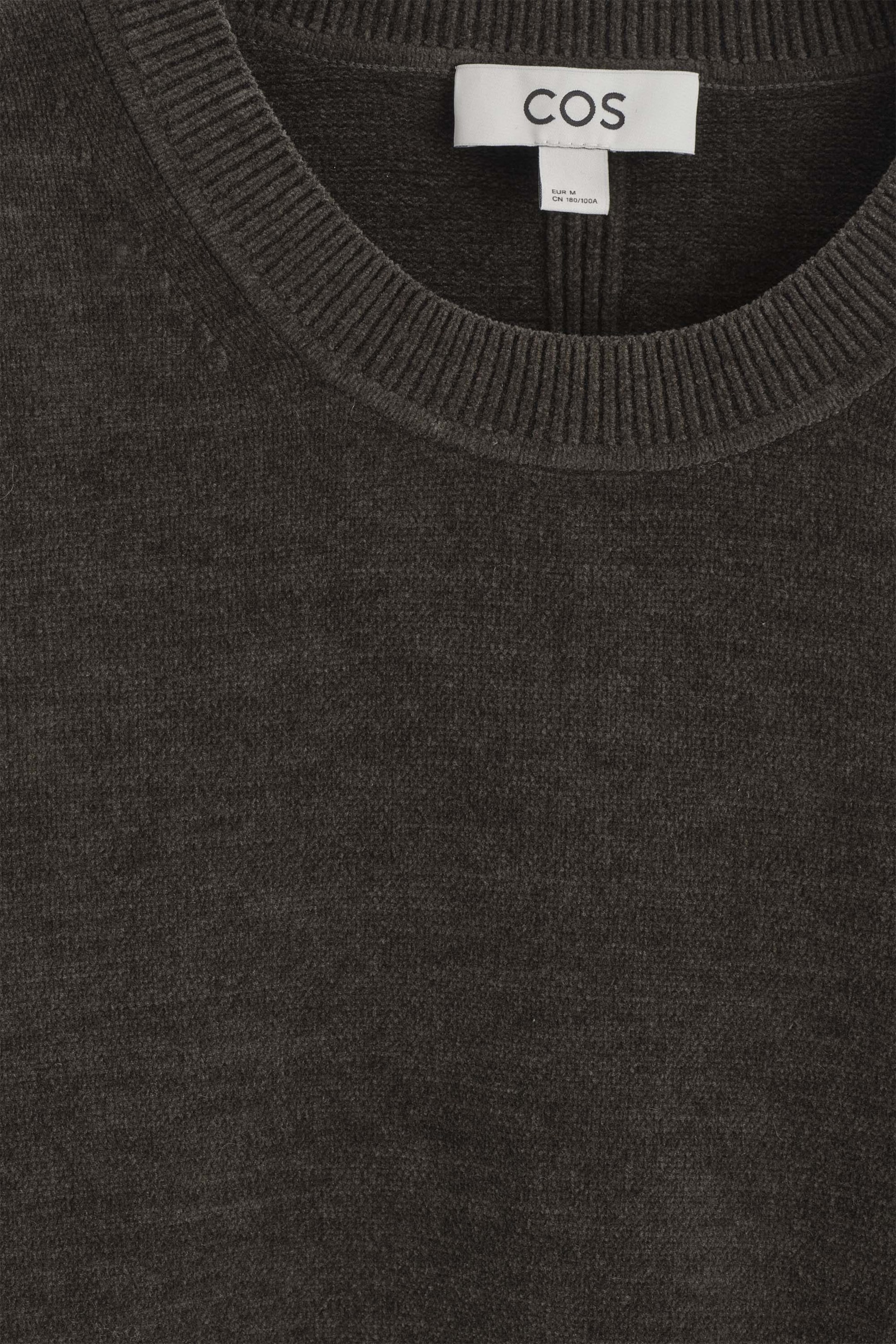A dark gray cotton-chenille crewneck sweater features a soft, textured knit fabric and a prominent ribbed collar. A white brand label is visible inside the back neckline of the garment. A dark gray cotton-chenille crewneck sweater features a soft, textured knit fabric and a prominent ribbed collar. A white brand label is visible inside the back neckline of the garment.