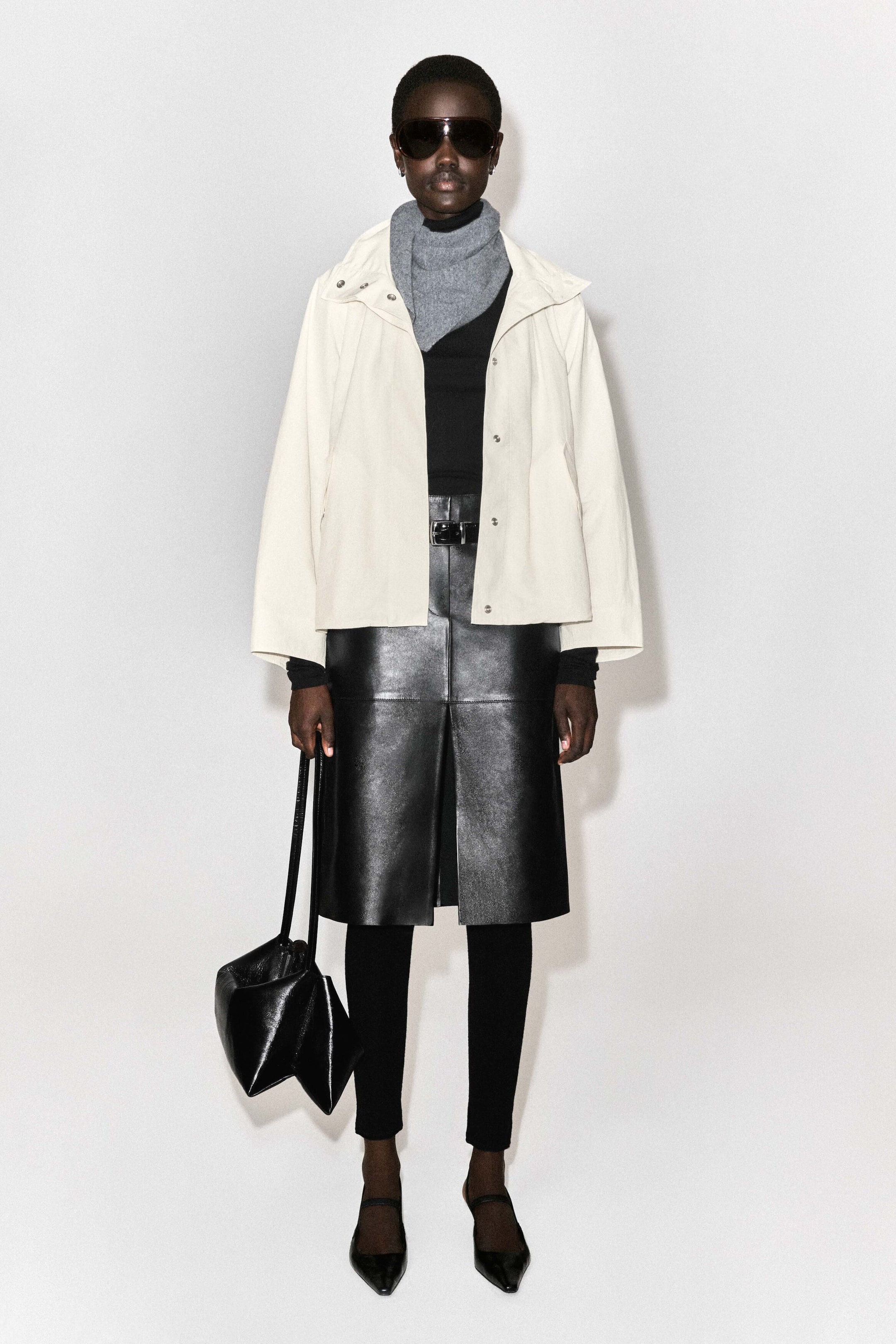 La veste à col cheminée en nylon est montrée de face dans une couleur blanc cassé, avec une silhouette carrée et courte, ainsi que des manches larges et décontractées. Elle est portée ouverte sur une écharpe grise et un haut noir, mettant en valeur son large col et ses fermetures à boutons-pression argentés le long de la patte de boutonnage avant. La veste à col cheminée en nylon est montrée de face dans une couleur blanc cassé, avec une silhouette carrée et courte, ainsi que des manches larges et décontractées. Elle est portée ouverte sur une écharpe grise et un haut noir, mettant en valeur son large col et ses fermetures à boutons-pression argentés le long de la patte de boutonnage avant.