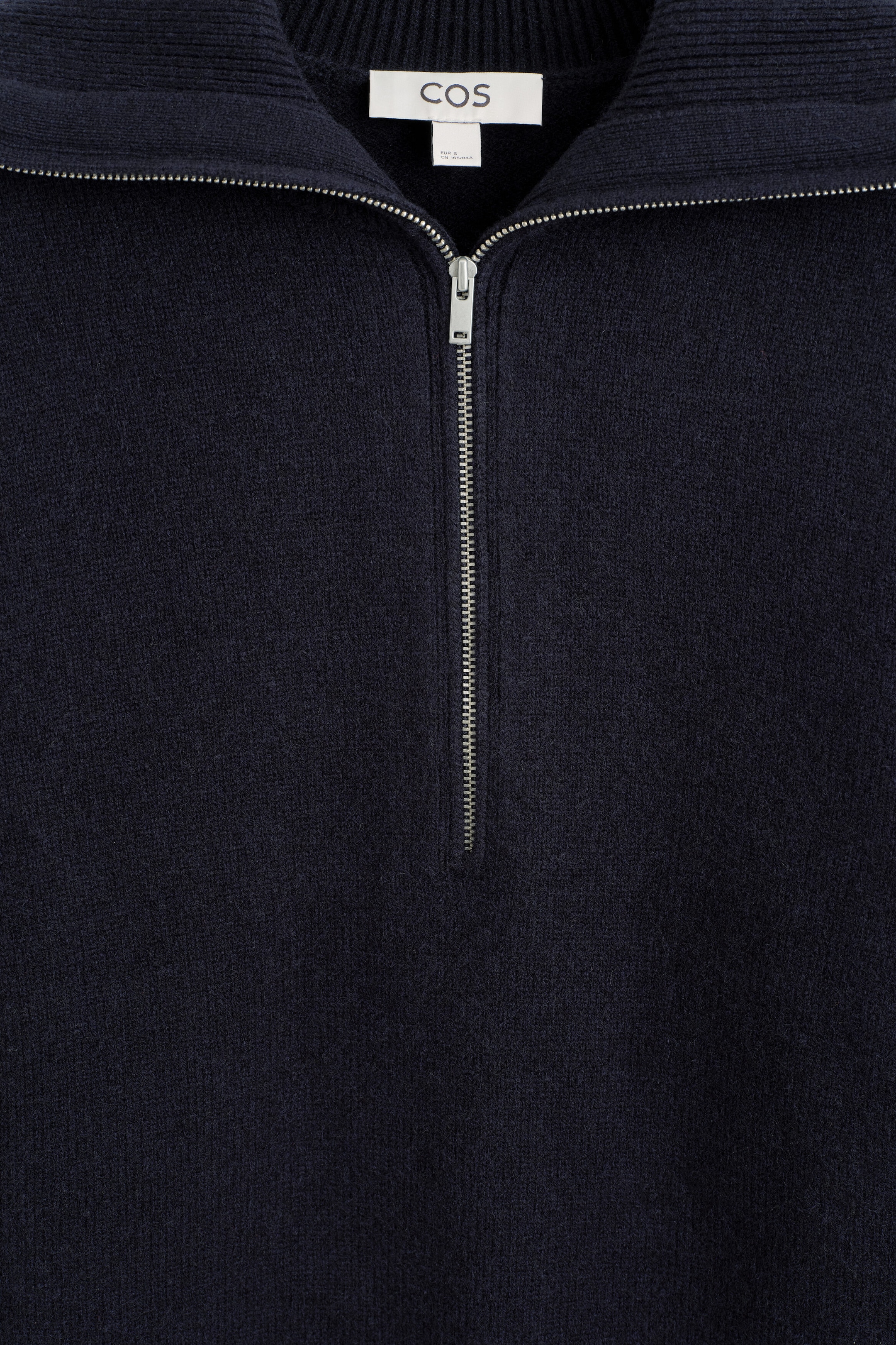 This navy blue knit jumper is showcasing its front design, featuring a ribbed collar and a silver-tone half-zip fastening. The white COS brand label is visible on the inner back neckline.