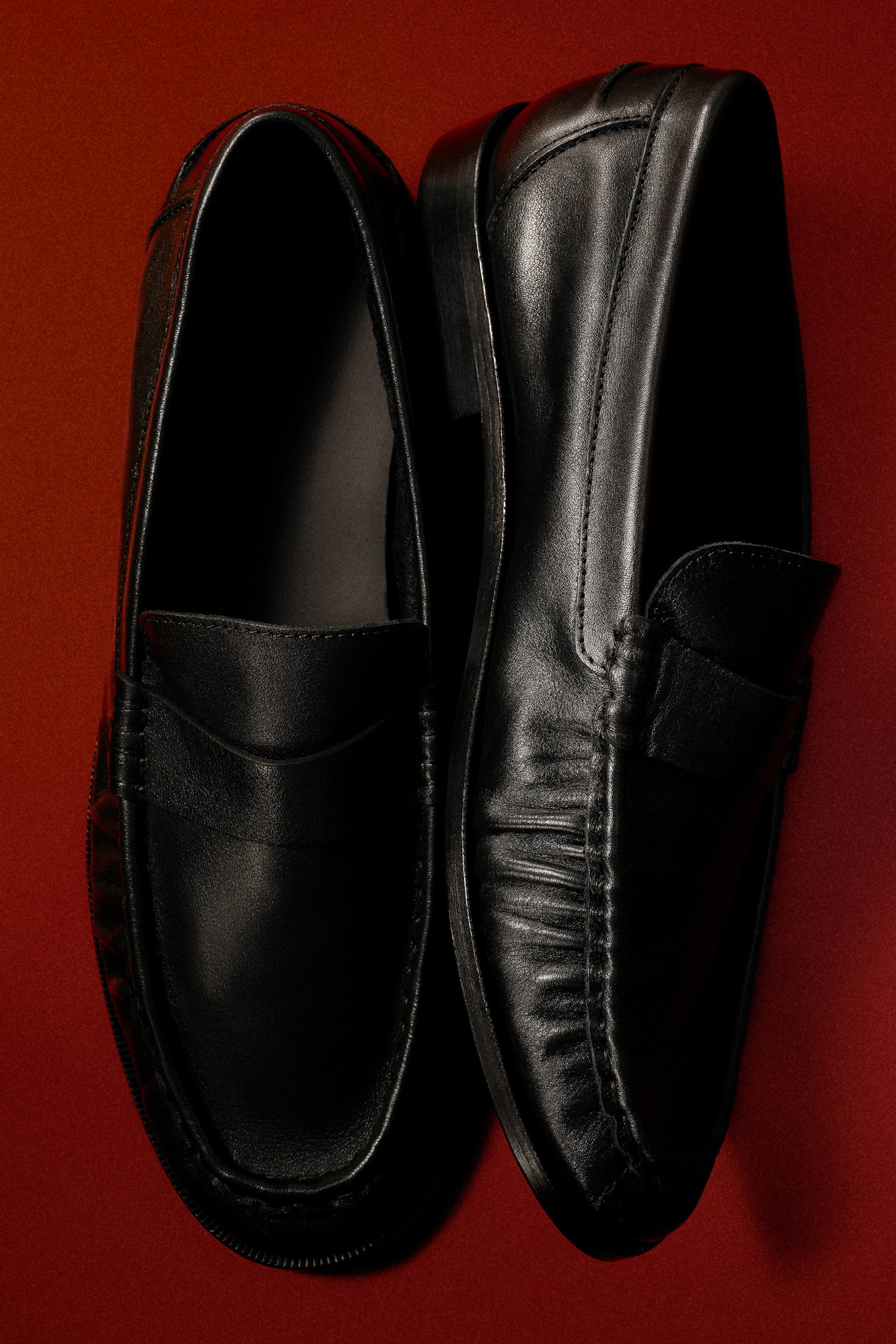 View larger image: A pair of black leather penny loafers is shown from a top-down perspective, showcasing their slip-on design. The loafers feature a classic penny strap across the vamp, softly ruched leather along the side seams, and a low block heel.