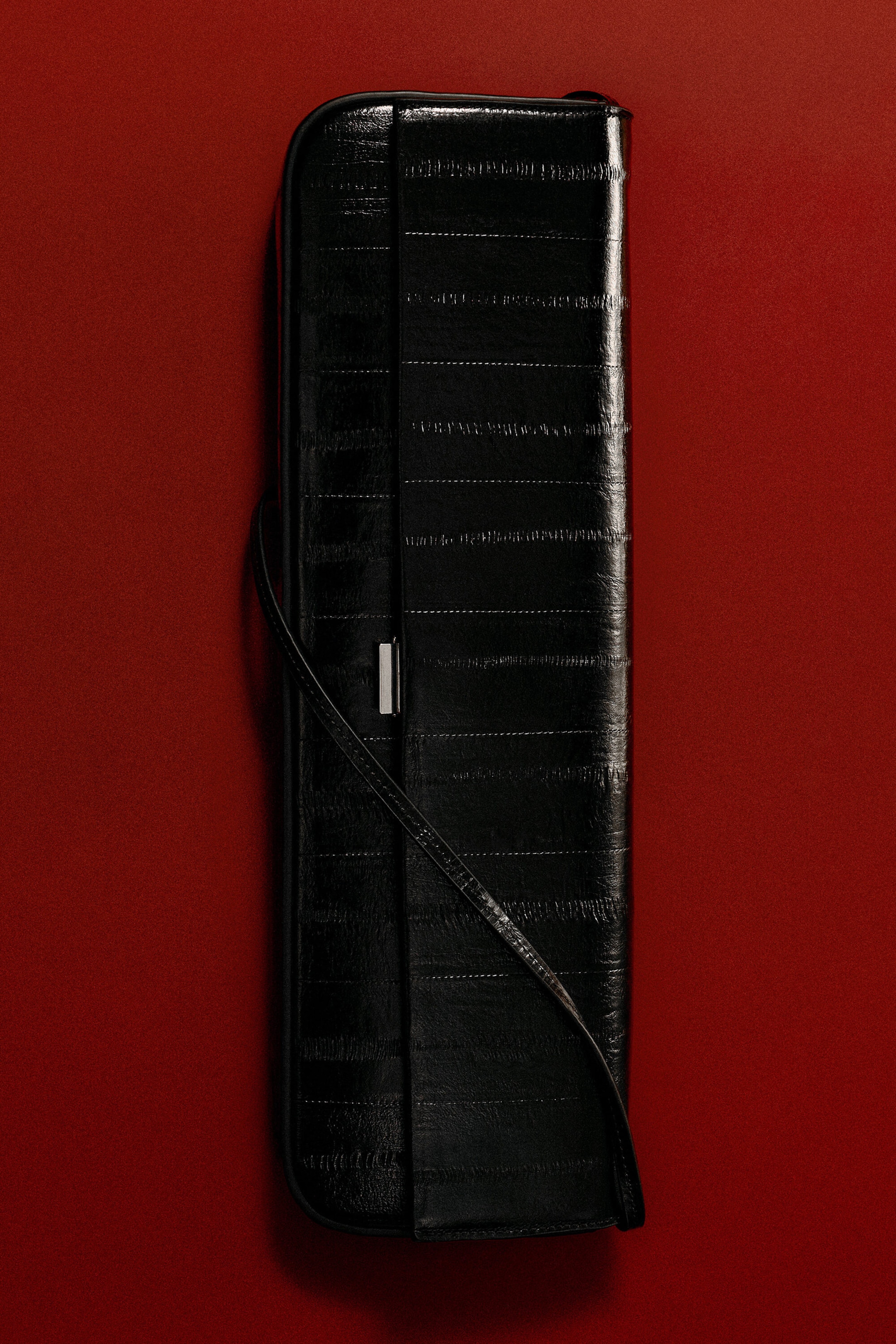The black eel-effect leather Parquet Clutch Bag features a slim, elongated rectangular design with horizontal panel stitching. A thin, matching leather strap drapes across the front, accented by a small silver-tone metal clasp along the opening edge. The black eel-effect leather Parquet Clutch Bag features a slim, elongated rectangular design with horizontal panel stitching. A thin, matching leather strap drapes across the front, accented by a small silver-tone metal clasp along the opening edge.