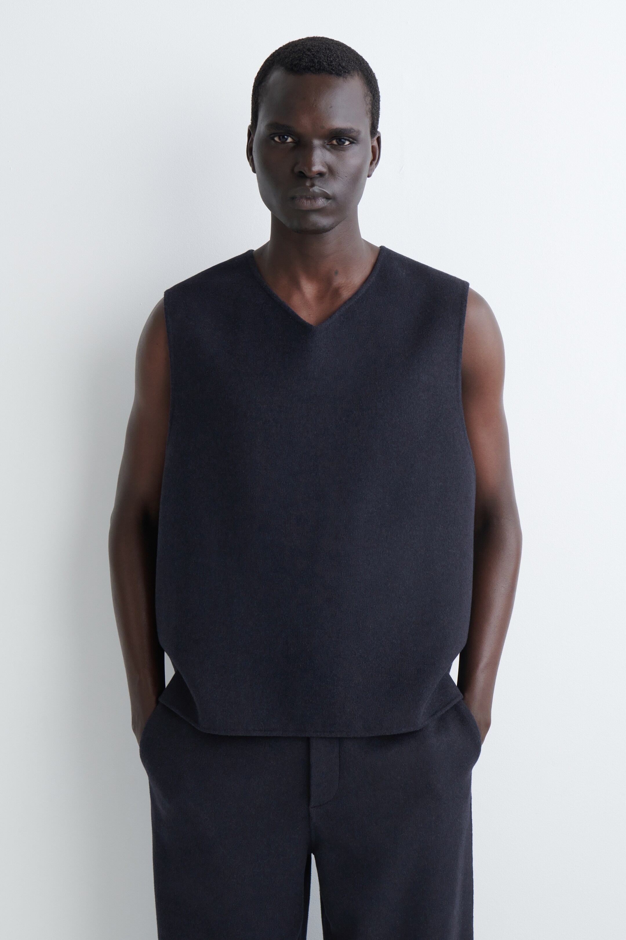 Agrandir l'image: Un haut en maille sans manches à encolure en V, de coupe ample et de couleur sombre, est présenté face avant, mettant en valeur une texture lisse et sombre, et est montré avec un pantalon assorti en maille sombre.