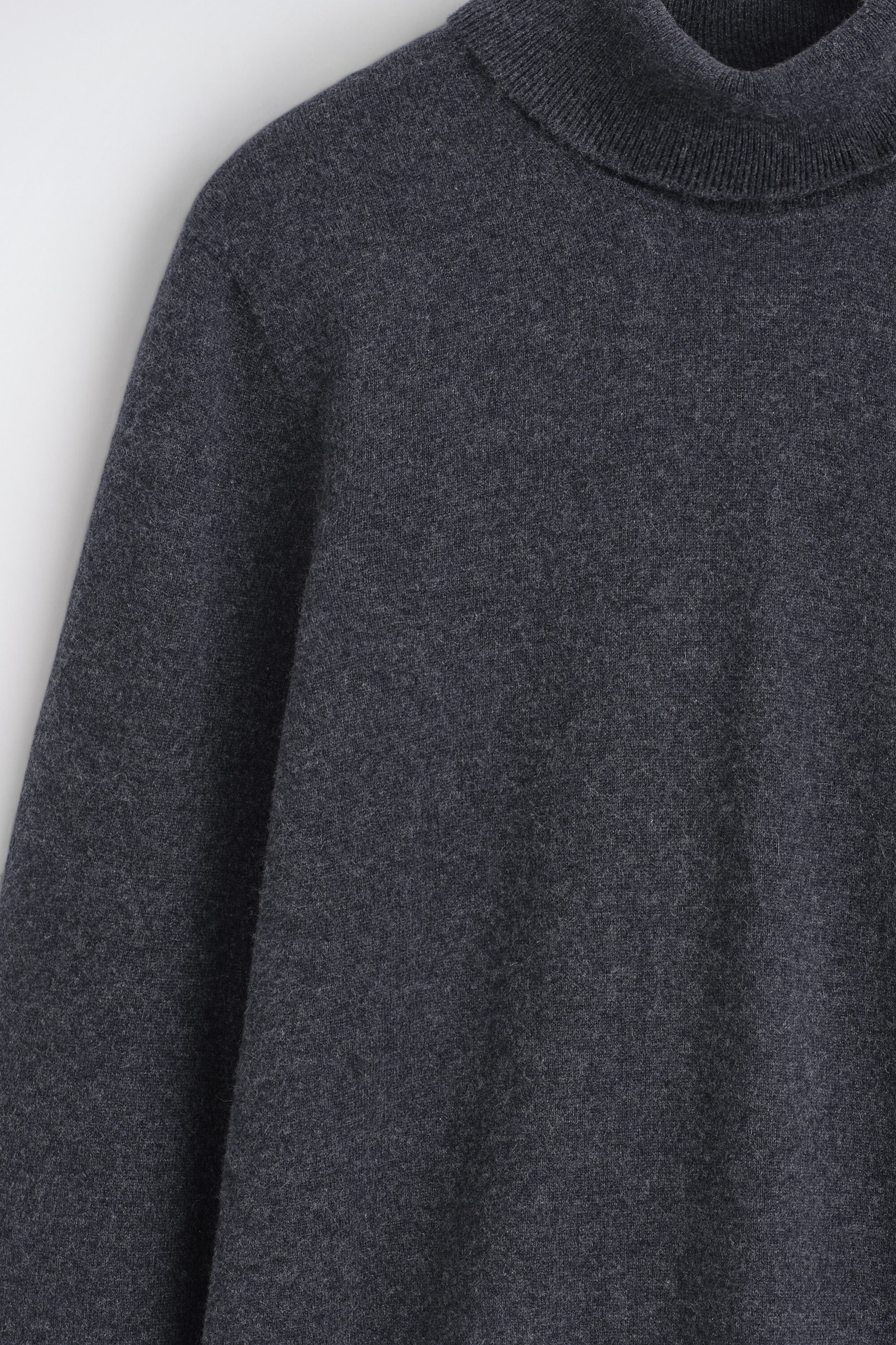 Un pull à col roulé en pur cachemire gris foncé présente un col roulé côtelé et une texture fine et douce en maille, vu de face en gros plan. Un pull à col roulé en pur cachemire gris foncé présente un col roulé côtelé et une texture fine et douce en maille, vu de face en gros plan.