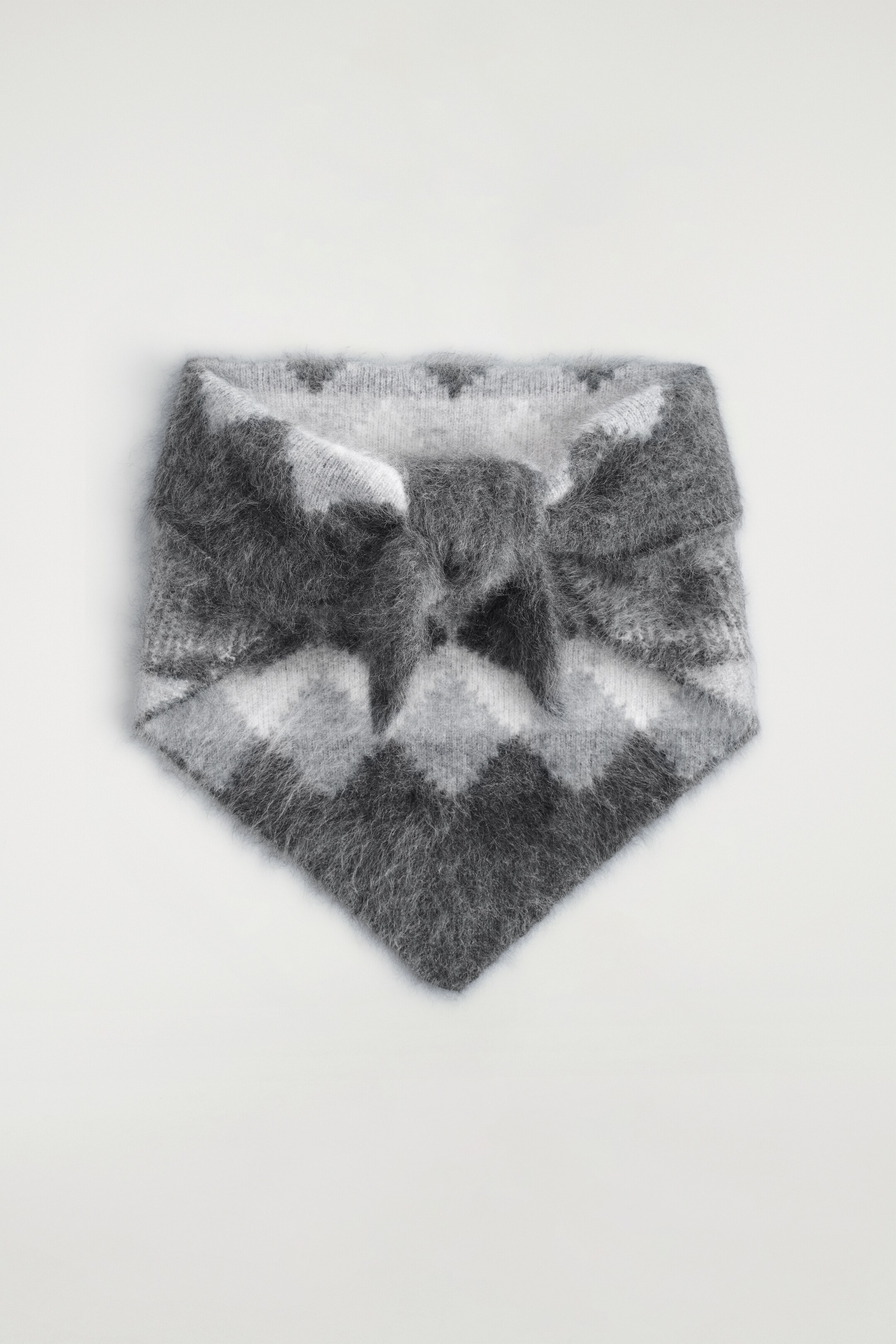 Ver imagen más grande: Un pañuelo triangular de cachemira suavemente cepillado, visto desde el frente, presenta un patrón de tejido intarsia Fairisle en tonos grises y está atado con un nudo en el centro.