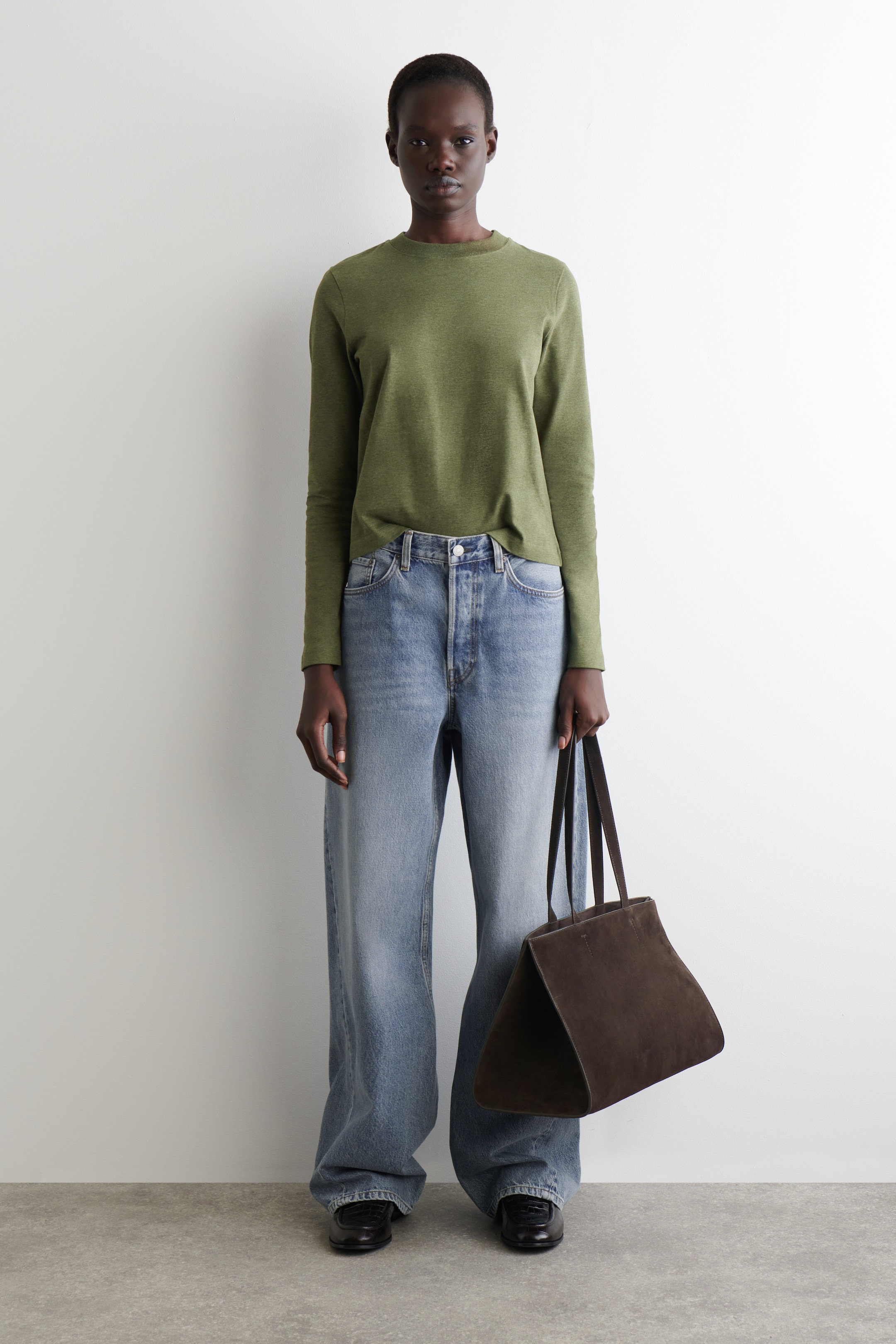 Visualizza immagine più grande: Una maglia a maniche lunghe verde oliva mélange è presentata, rivolta in avanti. Presenta un girocollo e una vestibilità rilassata, con l'orlo dritto che poggia liberamente su jeans in denim a lavaggio chiaro.
