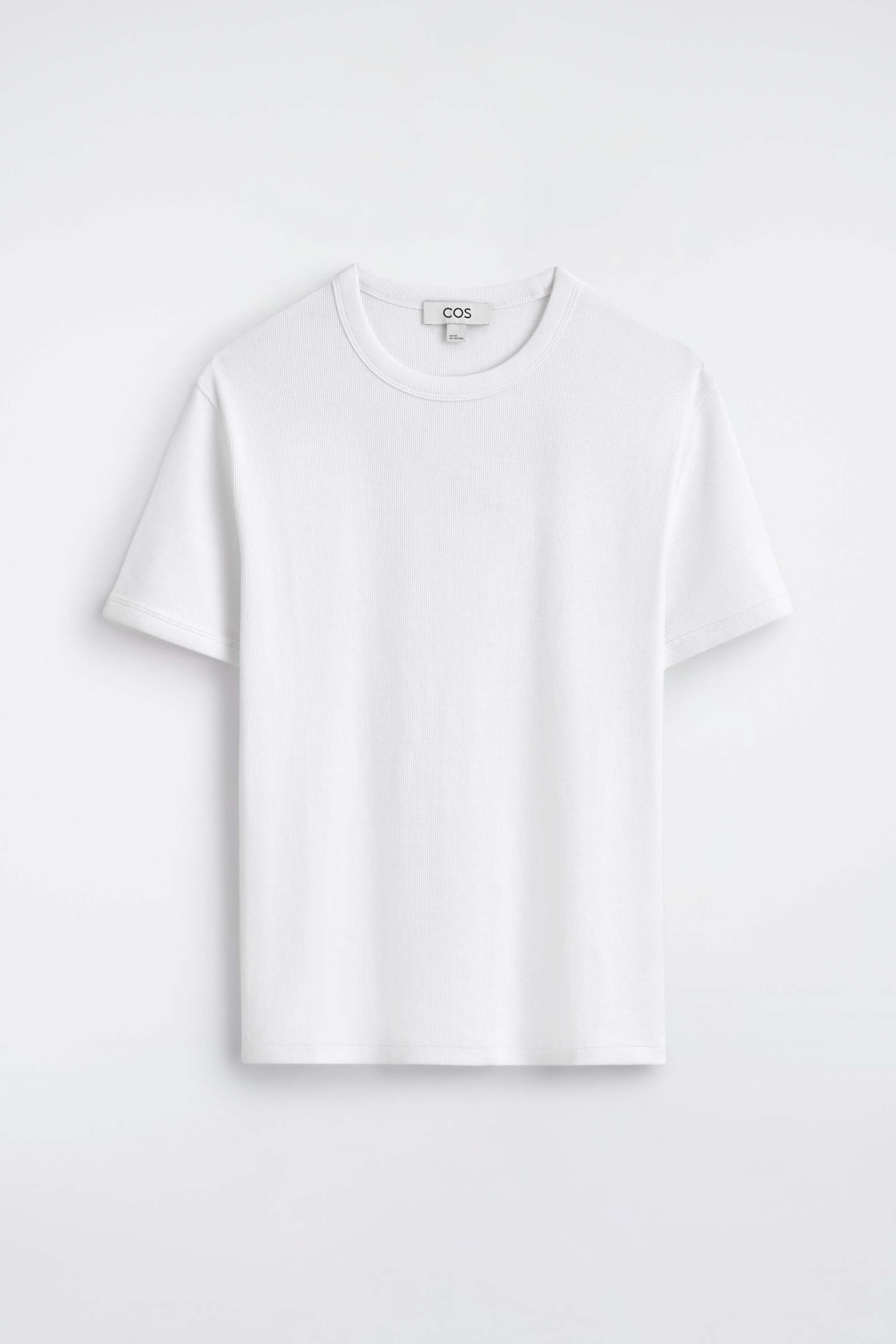 The slim ribbed cotton T-shirt is hanging front-facing, showcasing its fine ribbed texture, classic crew neck, and short sleeves. The white T-shirt displays a clean, structured silhouette with a brand label visible on the inner neckline.