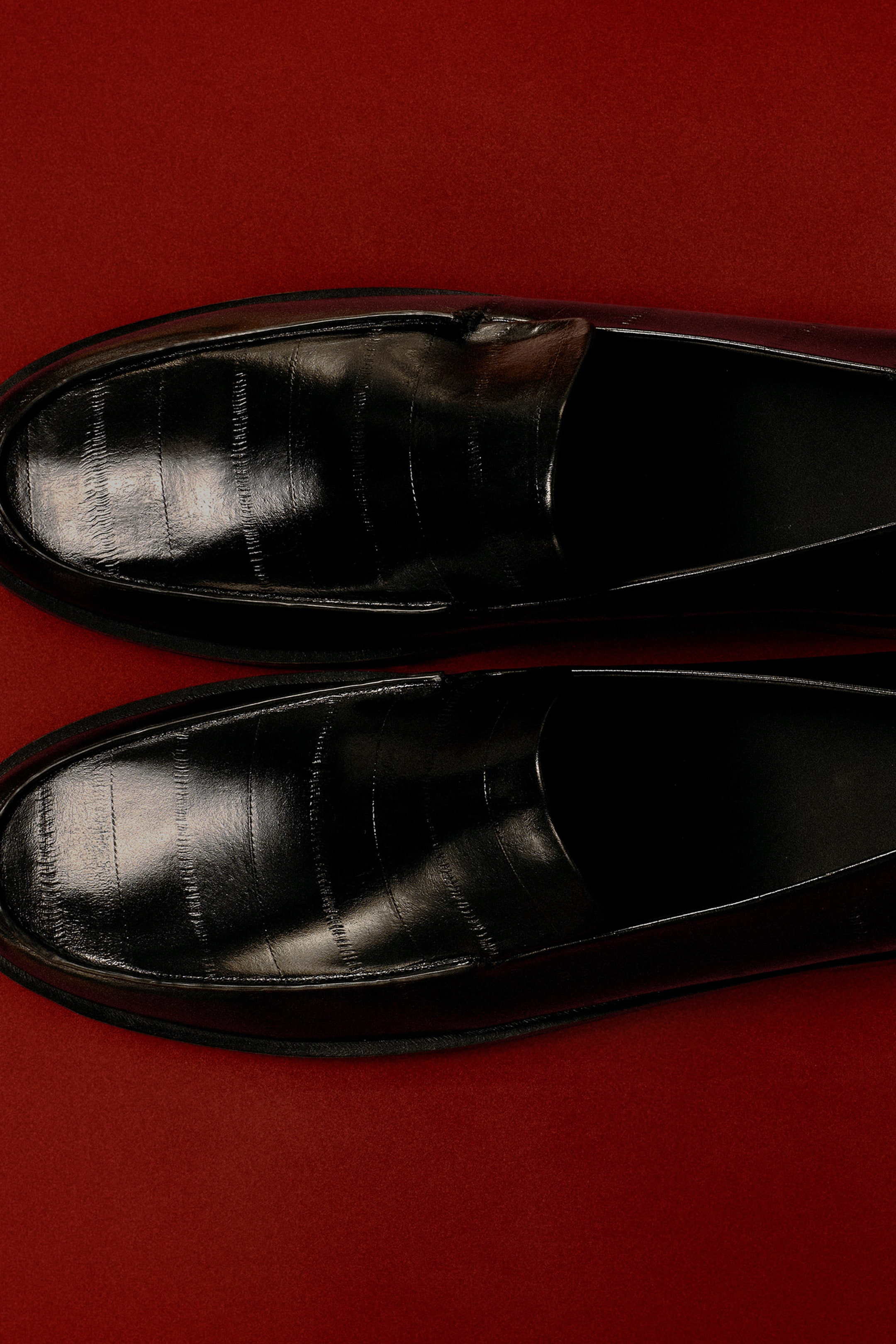 Agrandir l'image: Des mocassins en cuir noir poli sont présentés en vue de dessus, mettant en valeur leurs bouts arrondis et leur texture embossée distinctive effet anguille.