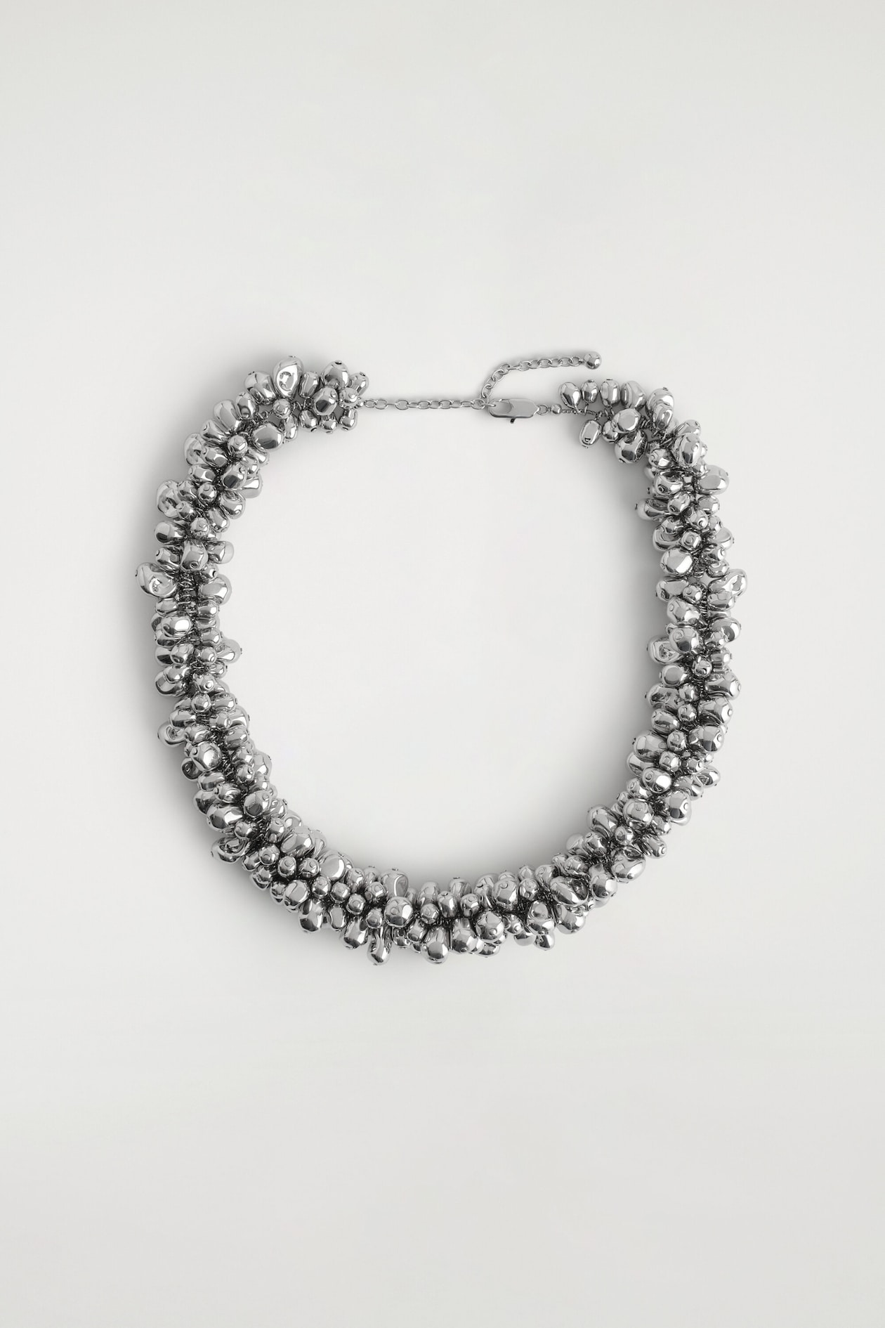 A front-facing view of a silver-tone necklace displaying a dense cluster of polished, organically shaped metallic spheres. The necklace is laid flat in a circular arrangement, showing an adjustable chain with a lobster clasp closure at the top.