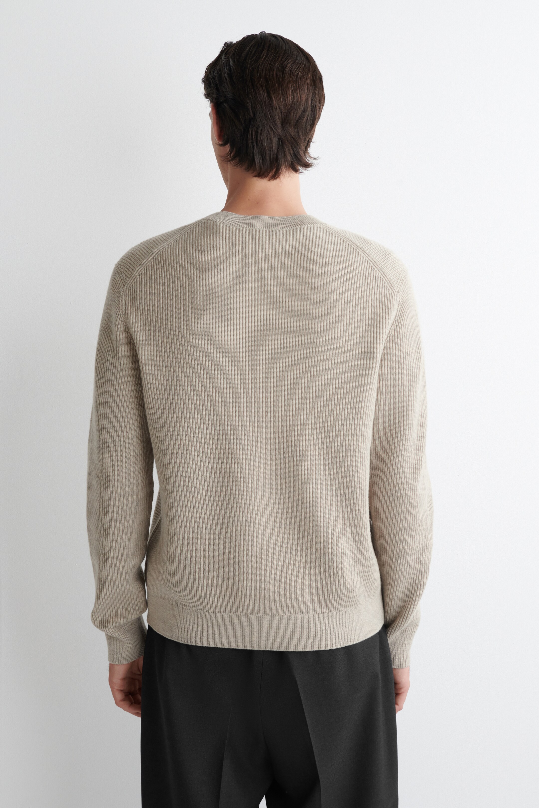 Agrandir l'image: Le pull beige est montré de dos, présentant une texture côtelée verticale régulière. Il est conçu avec un col rond, des manches raglan avec des poignets côtelés, et un ourlet côtelé.