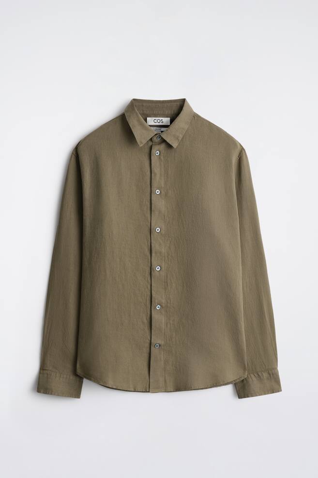 Una camicia verde smeraldo a maniche lunghe con vestibilità rilassata è presentata frontalmente, caratterizzata da un colletto a punta, una chiusura frontale completa con bottoni chiari, maniche lunghe con polsini e un orlo curvo. La camicia è realizzata in lino, mostrando una finitura leggermente testurizzata. - 1