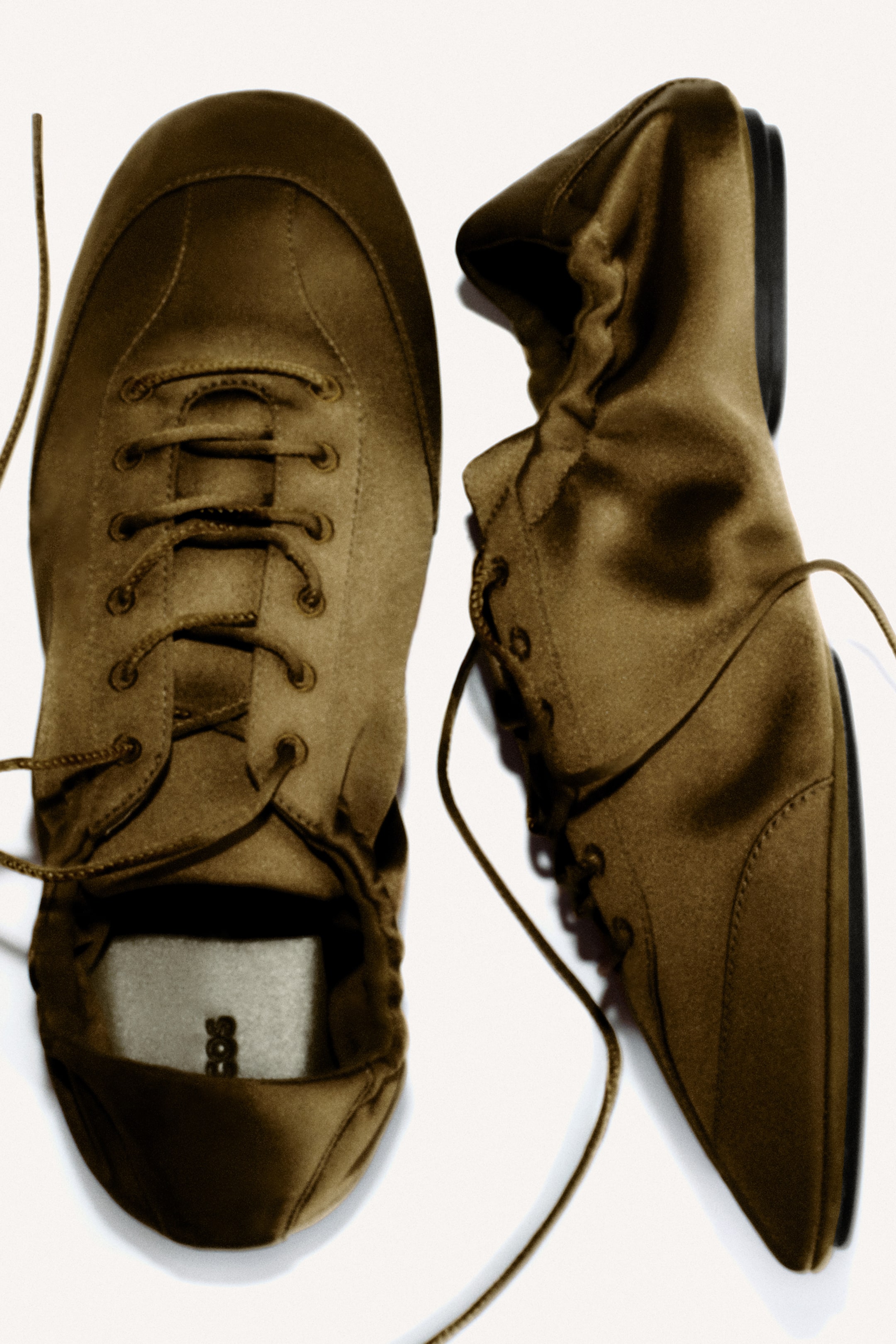 Agrandir l'image: Deux chaussures à lacets marron olive sont présentées. Une chaussure est orientée vers le haut, mettant en valeur son bout arrondi et ses lacets visibles, tandis que l'autre est posée sur le côté, affichant son profil avec une semelle noire fine et une ouverture à la cheville froncée.