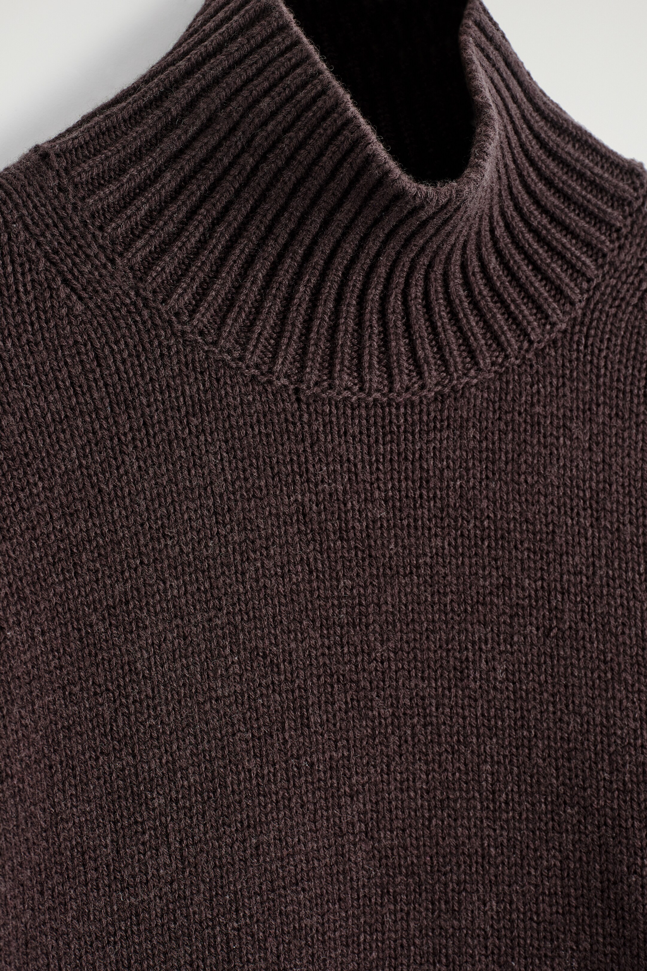 View larger image: A dark brown knitted jumper is featuring a chunky, ribbed funnel neck. The body of the jumper is knitted in a stockinette pattern.