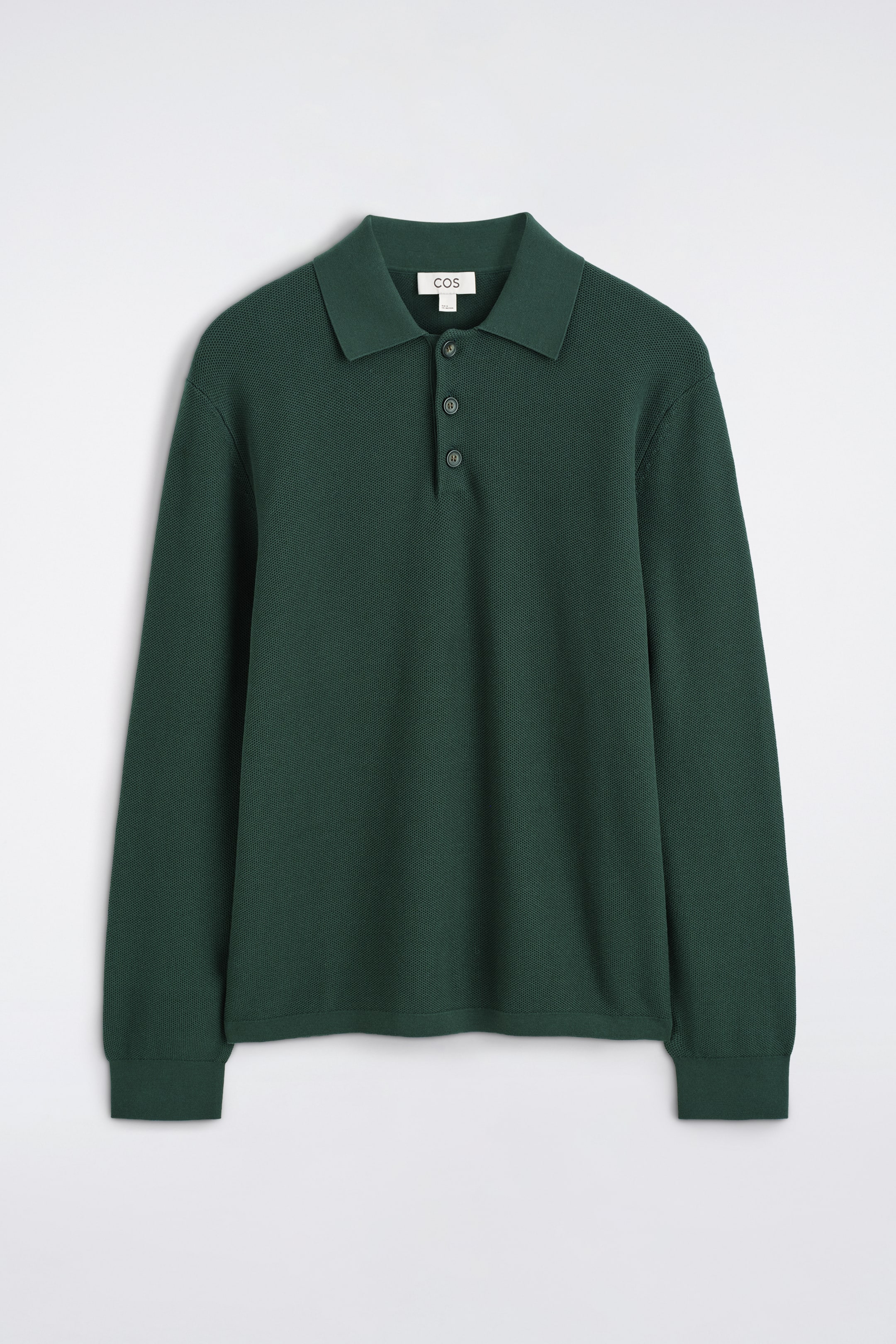 Größeres Bild ansehen: Ein dunkelgrünes langärmliges Poloshirt zeigt seine Vorderseite. Es präsentiert eine Wabenstrickstruktur, einen Polokragen und eine Dreiknopfleiste mit dunklen Knöpfen. Die langen Ärmel enden mit gerippten Bündchen.