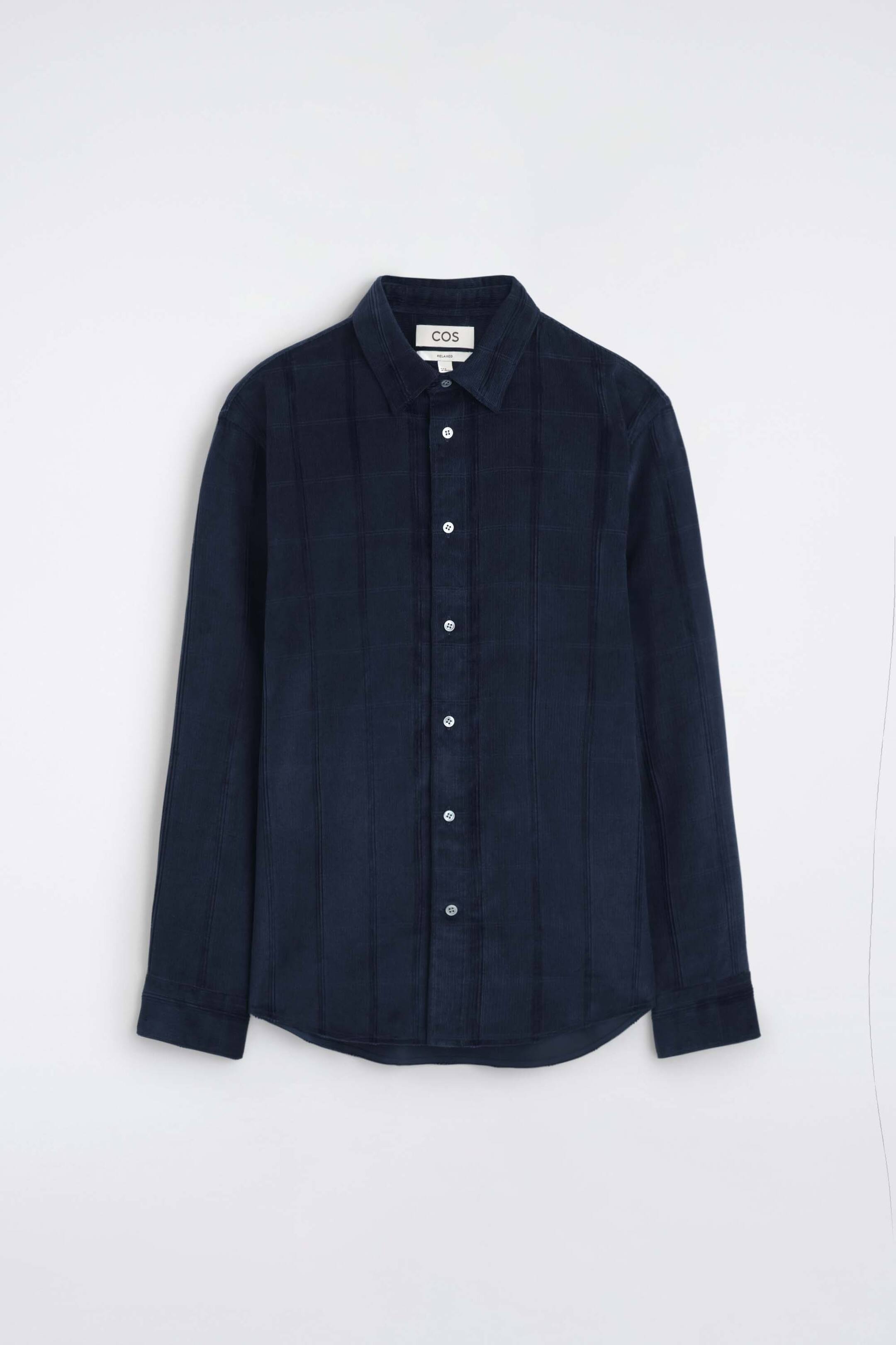 Visualizza l'immagine ingrandita: La camicia relaxed in velluto a coste è rivolta frontalmente, mostrando un tessuto in velluto a coste blu navy scuro con una sottile texture a quadri. Presenta un colletto a punta, una chiusura centrale con bottoni a contrasto bianchi e maniche lunghe con polsini abbottonati.