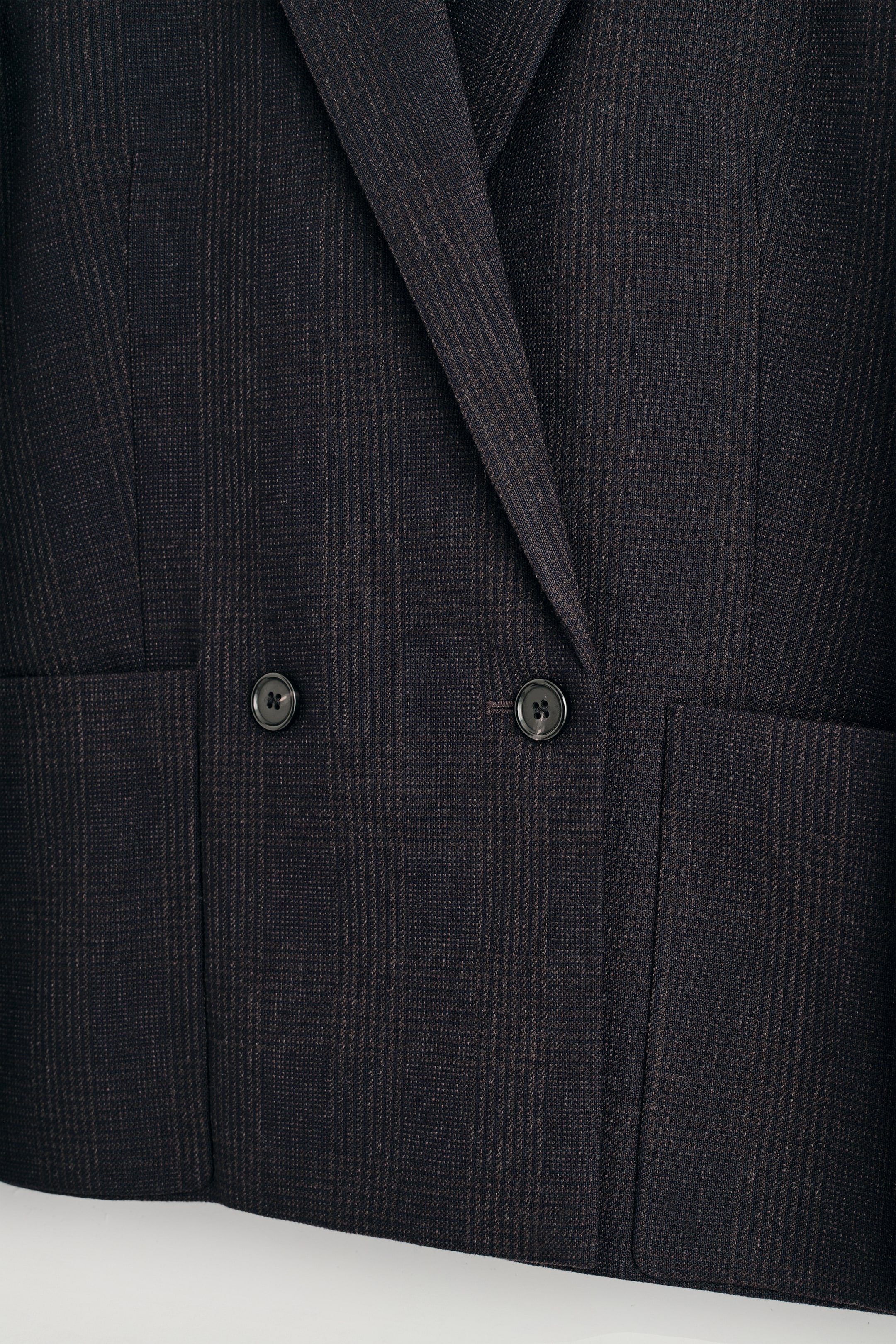 Se større billede: Forsiden af en dobbeltradet blazer viser et Prince of Wales ternmønster i espresso- og chokoladetoner. Den har en notch-lapel, to mørke firhuls knapper, en stor lappet lomme og en synlig lodret indsnitlinje.