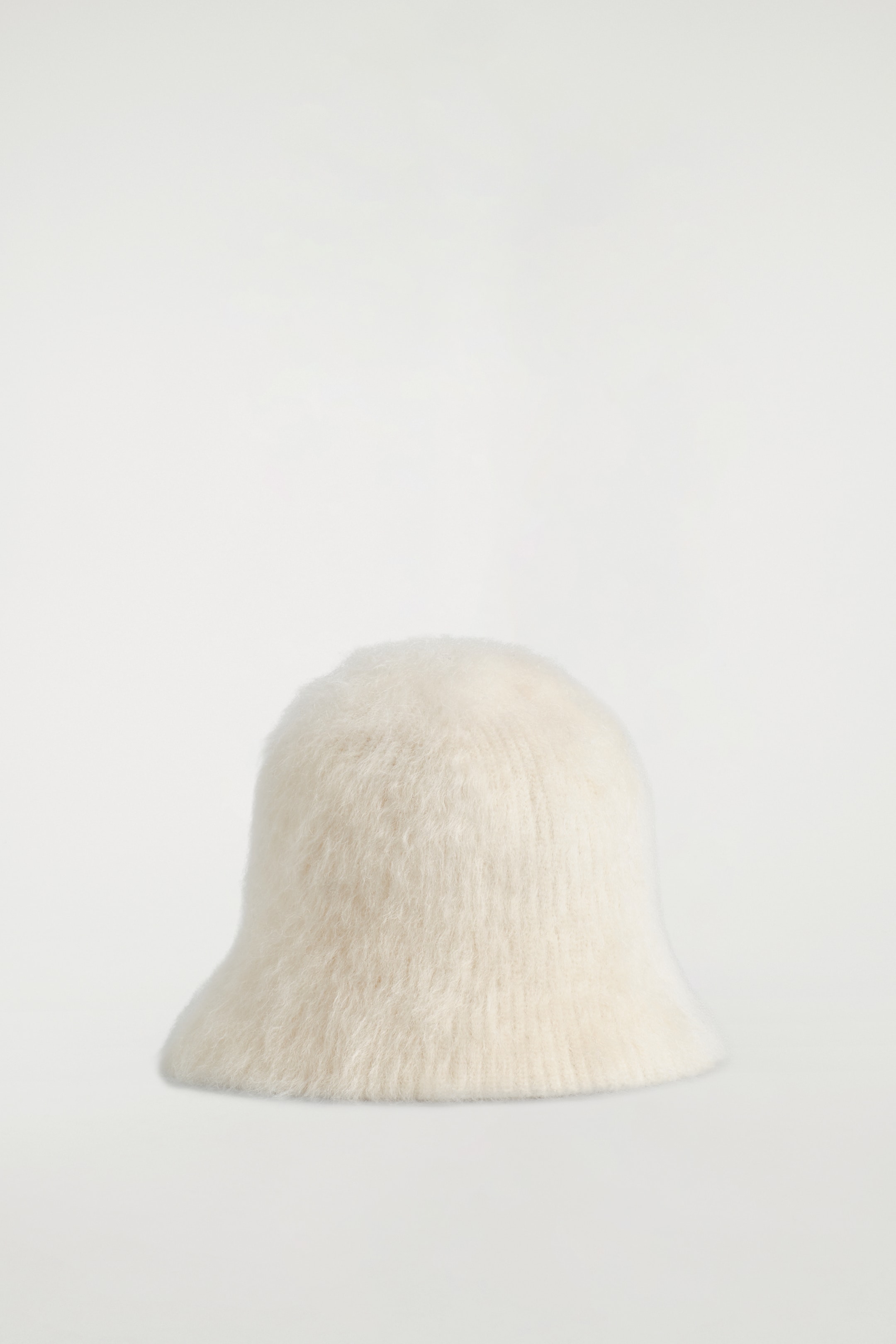 Agrandir l'image: Un chapeau à godets en tricot duveteux de couleur blanc cassé est présenté comme FRONT. Il présente une calotte arrondie et un bord subtilement étendu et incliné vers le bas, le tout confectionné dans un tricot à côtes visiblement texturé.
