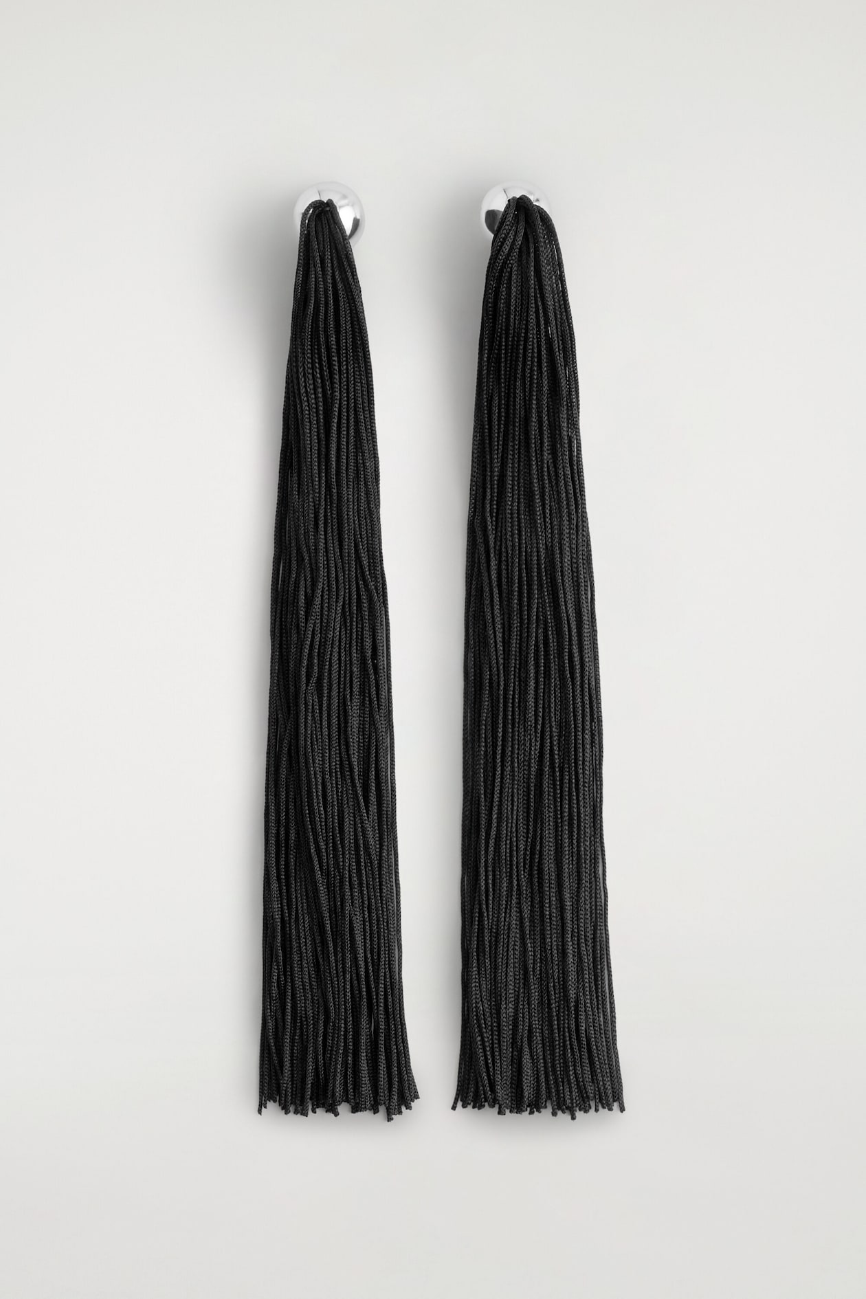 These fringed earrings are shown from the front, featuring silver-tone dome studs with long, dense black cord tassels hanging straight down.