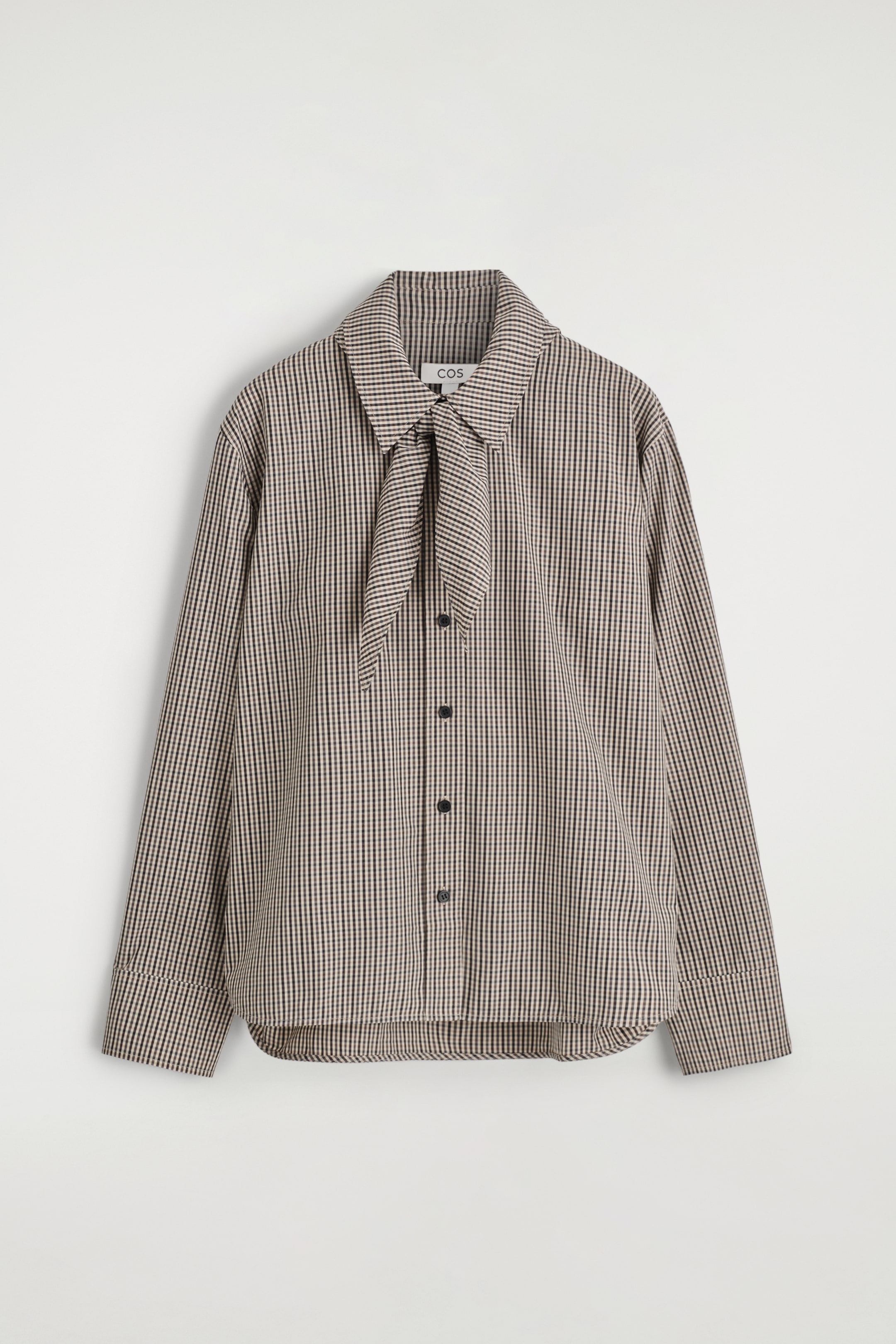 Agrandir l'image: VUE DE FACE. Une chemise à micro-carreaux marron, noir et crème présente un col pointu avec un détail de cravate intégré noué à l'avant. La chemise est conçue avec des manches longues, des poignets larges et une fermeture à boutons sur le devant avec des boutons foncés.