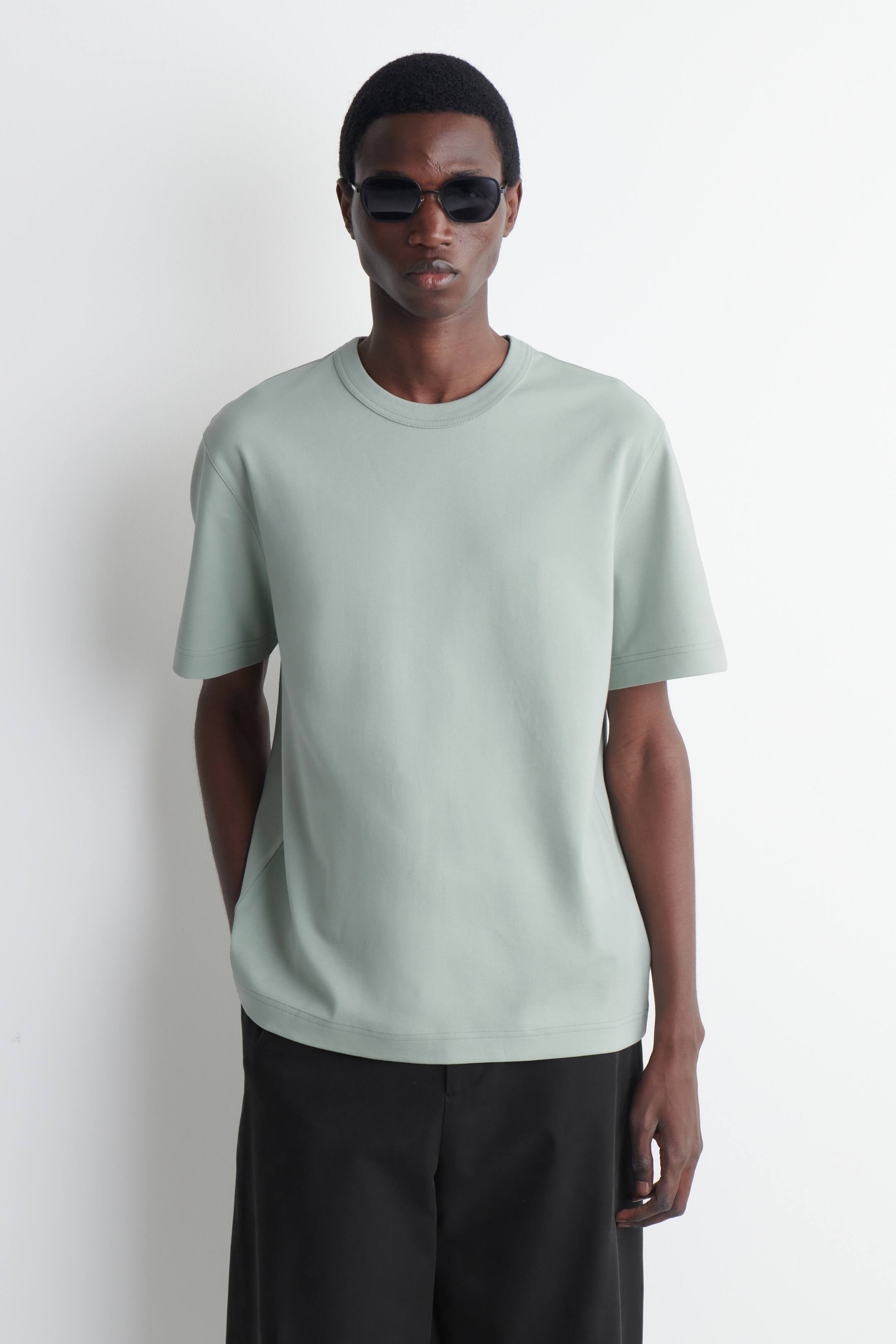 Agrandir l'image: Un T-shirt à col rond vert clair avec des manches courtes et une coupe décontractée est porté par le mannequin.