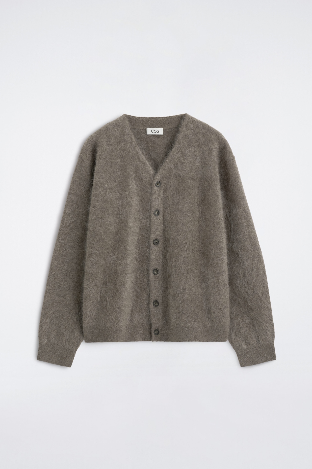 Ce cardigan à col en V en cachemire brossé est présenté de face, mettant en valeur son tricot duveteux et texturé dans une teinte taupe neutre. Le cardigan présente un profond col en V, une ouverture boutonnée sur le devant avec six boutons foncés et des manches longues avec poignets côtelés.