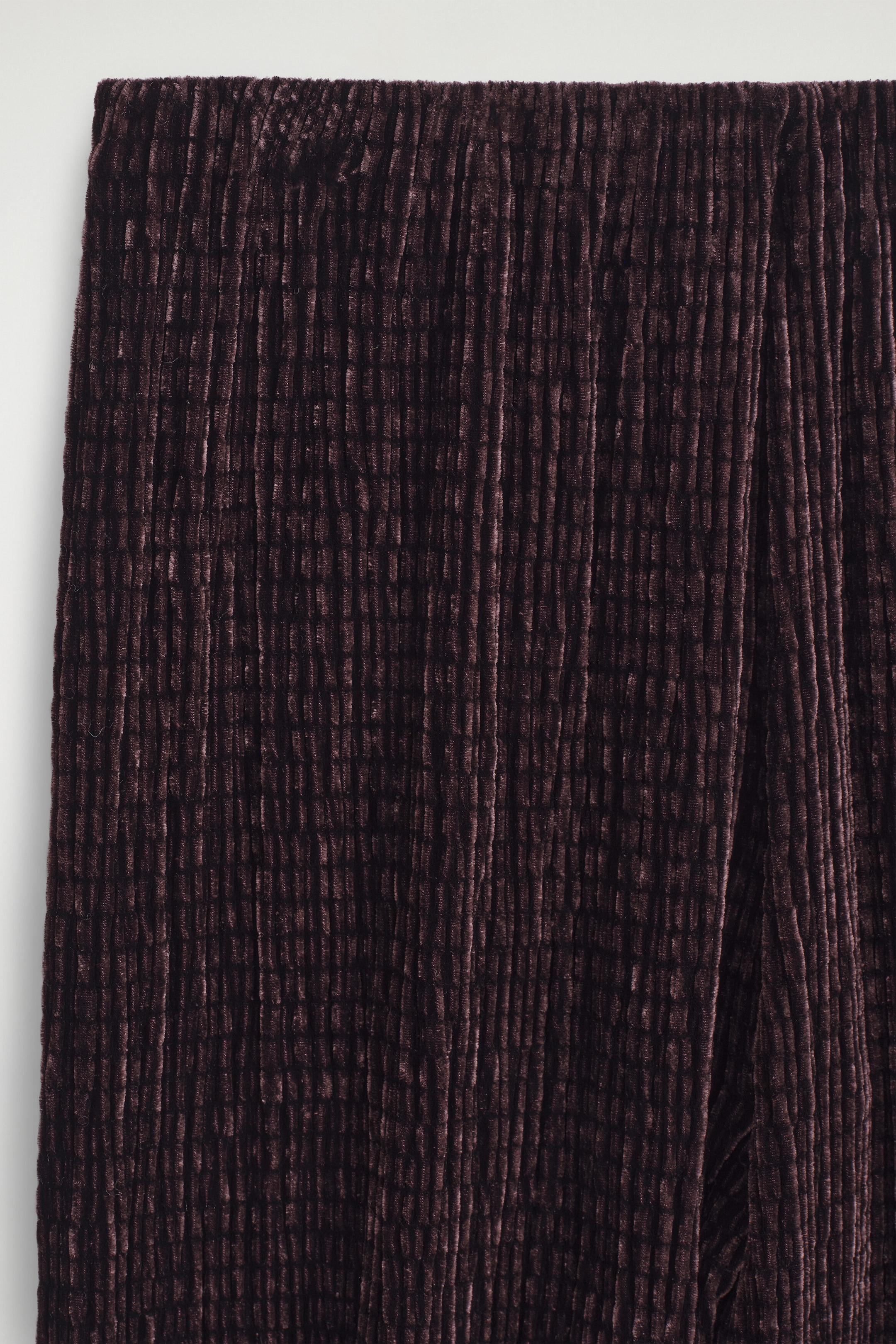 Dark plum trousers are shown in a close-up front view, featuring a plush, ribbed chenille-like texture and a flat elastic waistband. The fabric drapes straight down, emphasizing the vertical pleated pattern. Dark plum trousers are shown in a close-up front view, featuring a plush, ribbed chenille-like texture and a flat elastic waistband. The fabric drapes straight down, emphasizing the vertical pleated pattern.