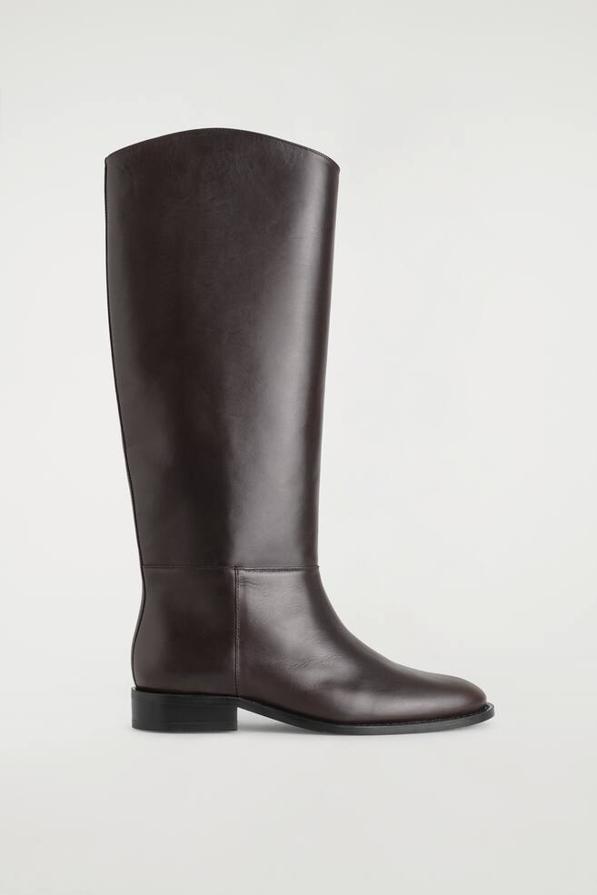A dark brown leather riding boot is standing in side profile facing right, featuring a tall, knee-high shaft with a sculpted topline, a rounded toe, and a low black block heel. - 1
