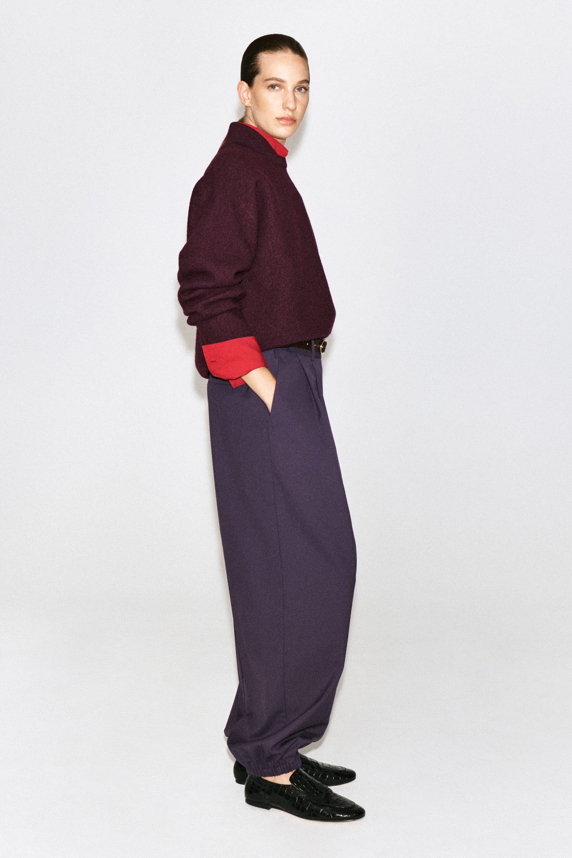 Un chandail en laine bouillie bourgogne, doté d’un col rouge superposé et de poignets assortis, est porté par le mannequin. Le chandail est agencé avec une sous-couche rouge à col montant et porté avec un pantalon pourpre foncé. Un chandail en laine bouillie bourgogne, doté d’un col rouge superposé et de poignets assortis, est porté par le mannequin. Le chandail est agencé avec une sous-couche rouge à col montant et porté avec un pantalon pourpre foncé.