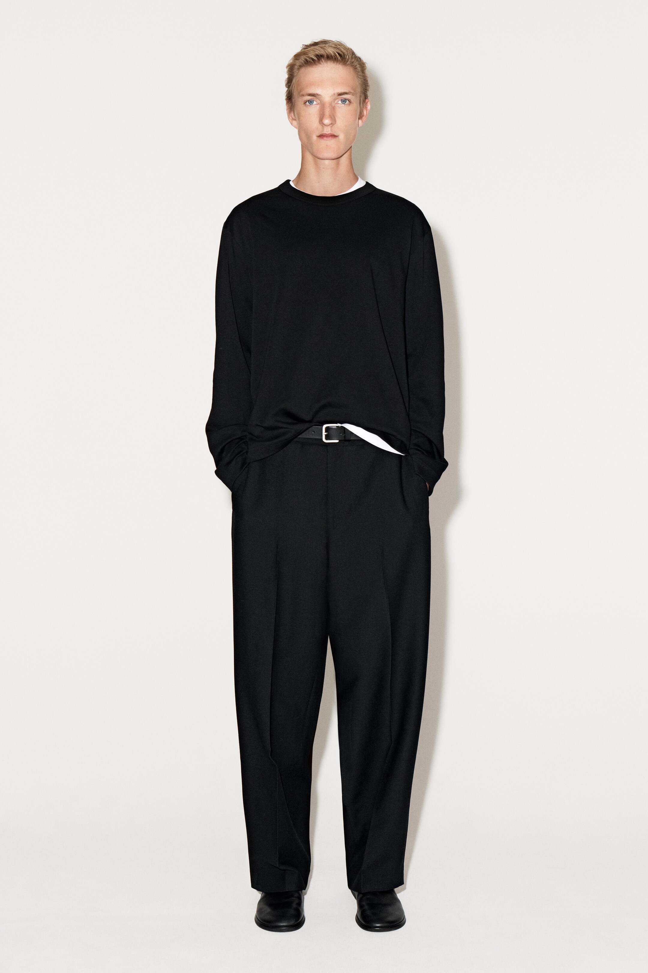 Agrandir l'image: Un T-shirt noir à manches longues est présenté de face, avec une coupe décontractée et un col rond classique. Une couche blanche est visible sous l'encolure et là où le T-shirt est rentré.