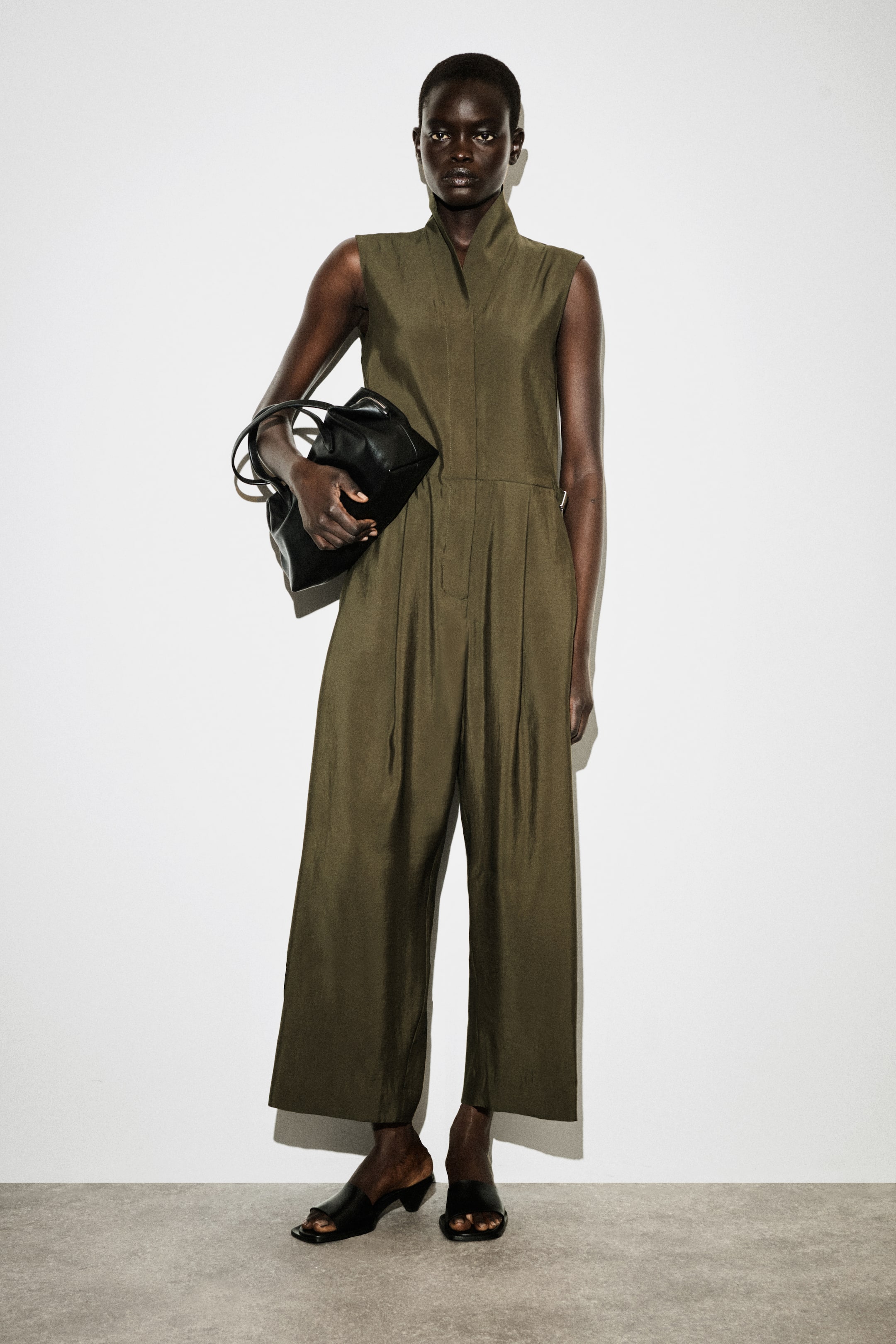 View larger image: An olive green jumpsuit featuring a sleeveless design, a high collar with a V-neck opening, and wide-leg pleated trousers, crafted from a fluid, drapey fabric.