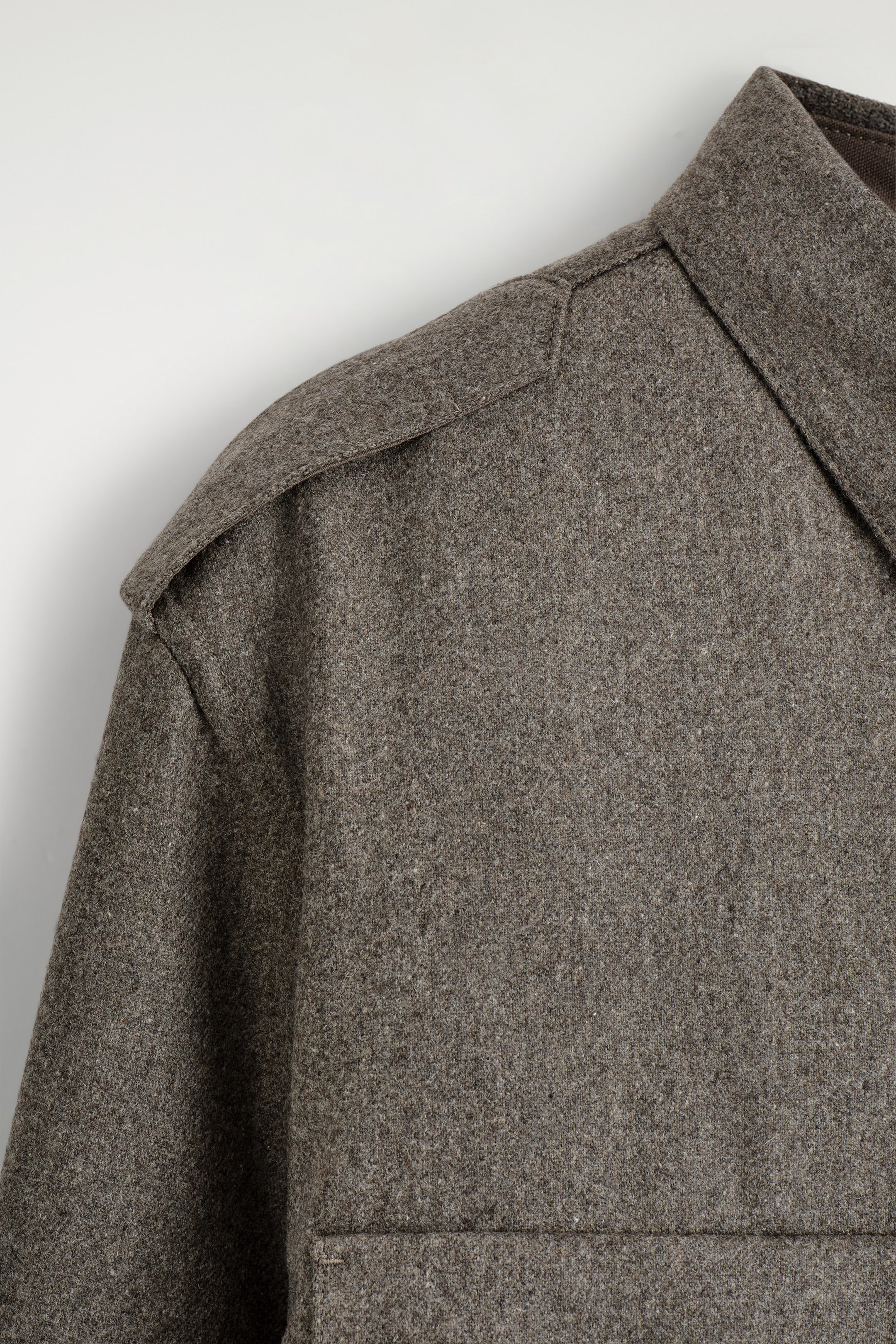 View larger image: A brown-grey utility shirt is shown in a close-up front view, highlighting its textured fabric. It is featuring an epaulette on the shoulder, a classic collar, and a partial view of a patch pocket at the bottom right.