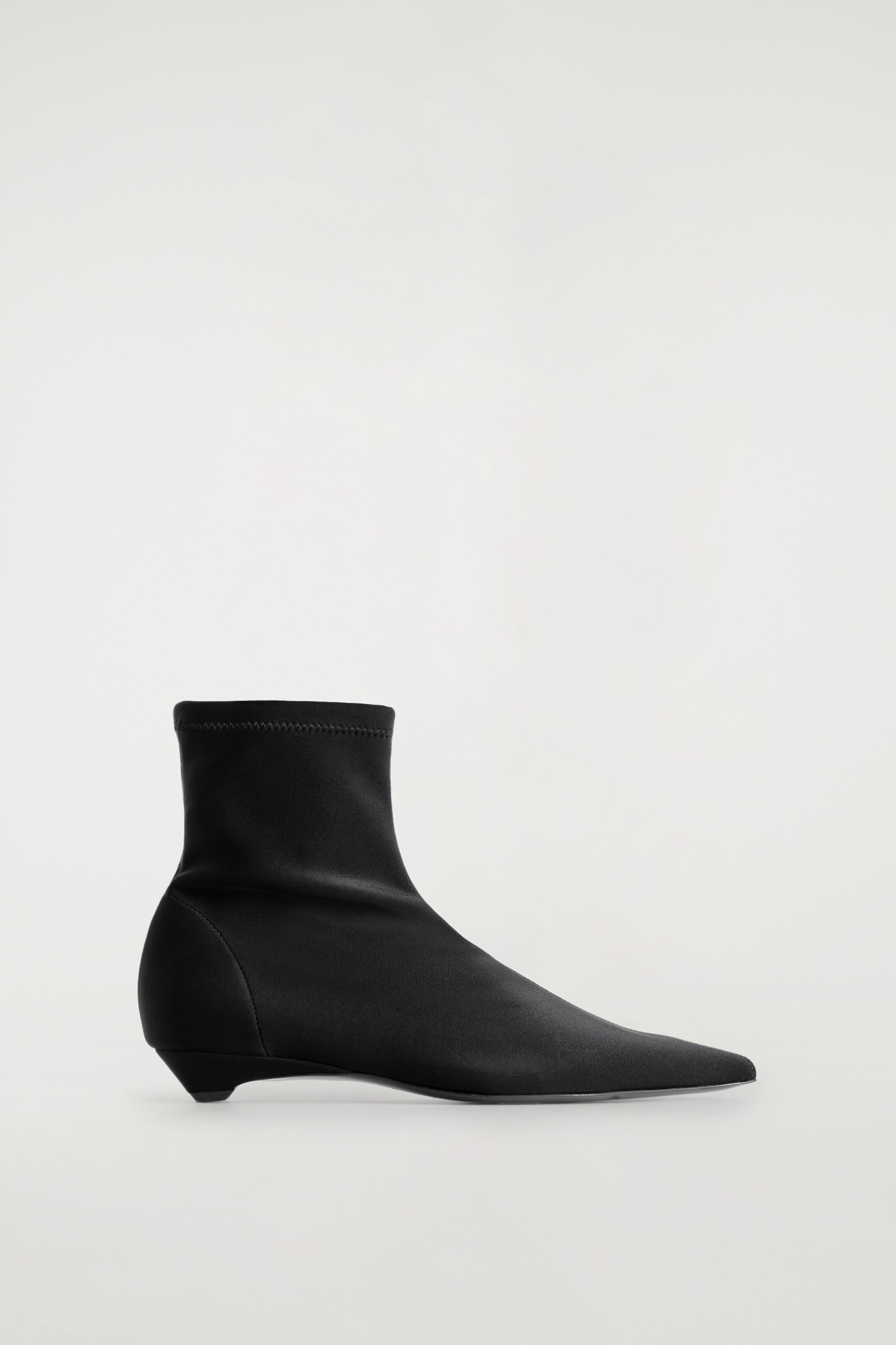 Größeres Bild ansehen: Ein schwarzer Sock-Boot zeigt sein RECHTES Profil, mit einer schlanken, knöchellangen Silhouette und einer spitzen Zehe. Er ist aus einem glatten, matten Material gefertigt, zeigt eine subtile Mittelnaht und wird von einem kleinen konischen Absatz unterstützt.