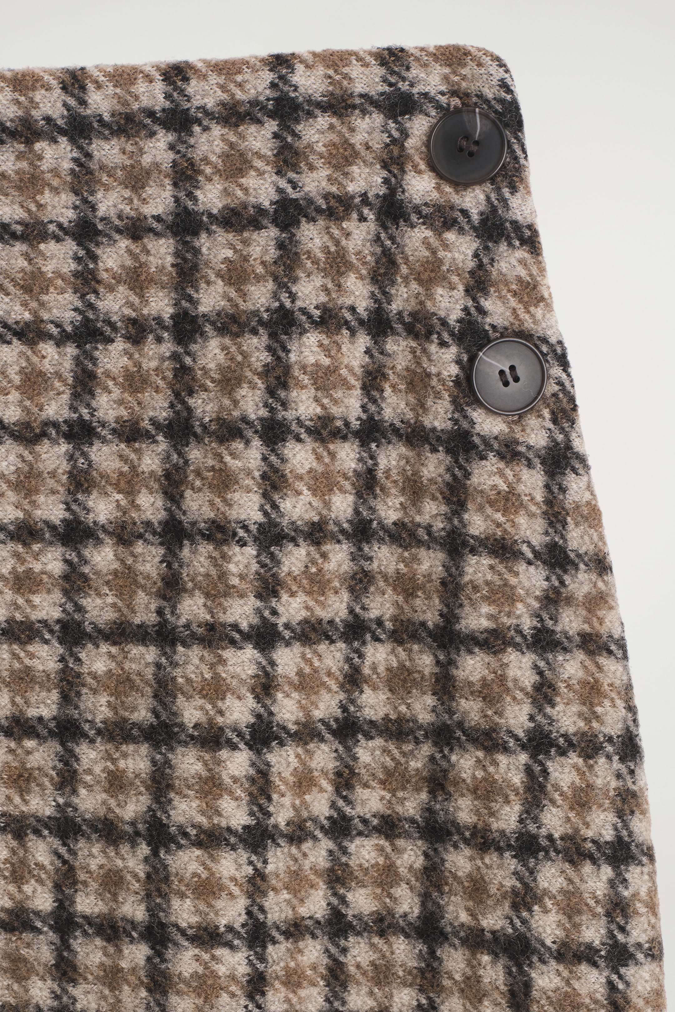 Grösseres Bild ansehen: Ein braun-beige-schwarz kariertes Hahnentritt-Muster zeigt eine strukturierte Webart, mit zwei dunkelgrauen, vierlochigen Knöpfen, die vertikal auf der oberen rechten Seite angeordnet sind.