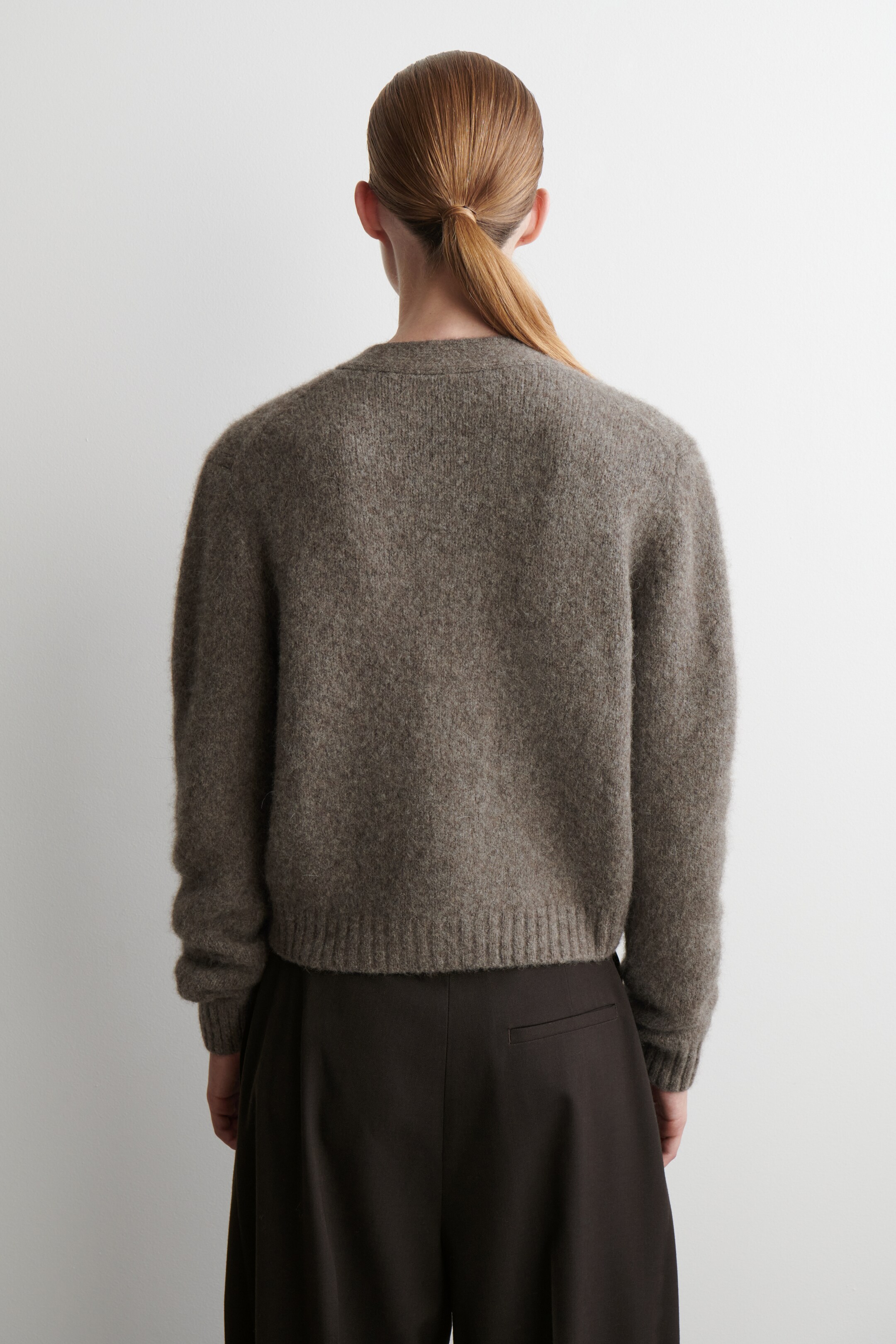 Se større billede: En brun-grå sweater vises fra bagsiden. Den har en blød tekstur, en rund hals, ribbede manchetter og en ribbet kant, hvilket giver en afslappet, kort pasform.