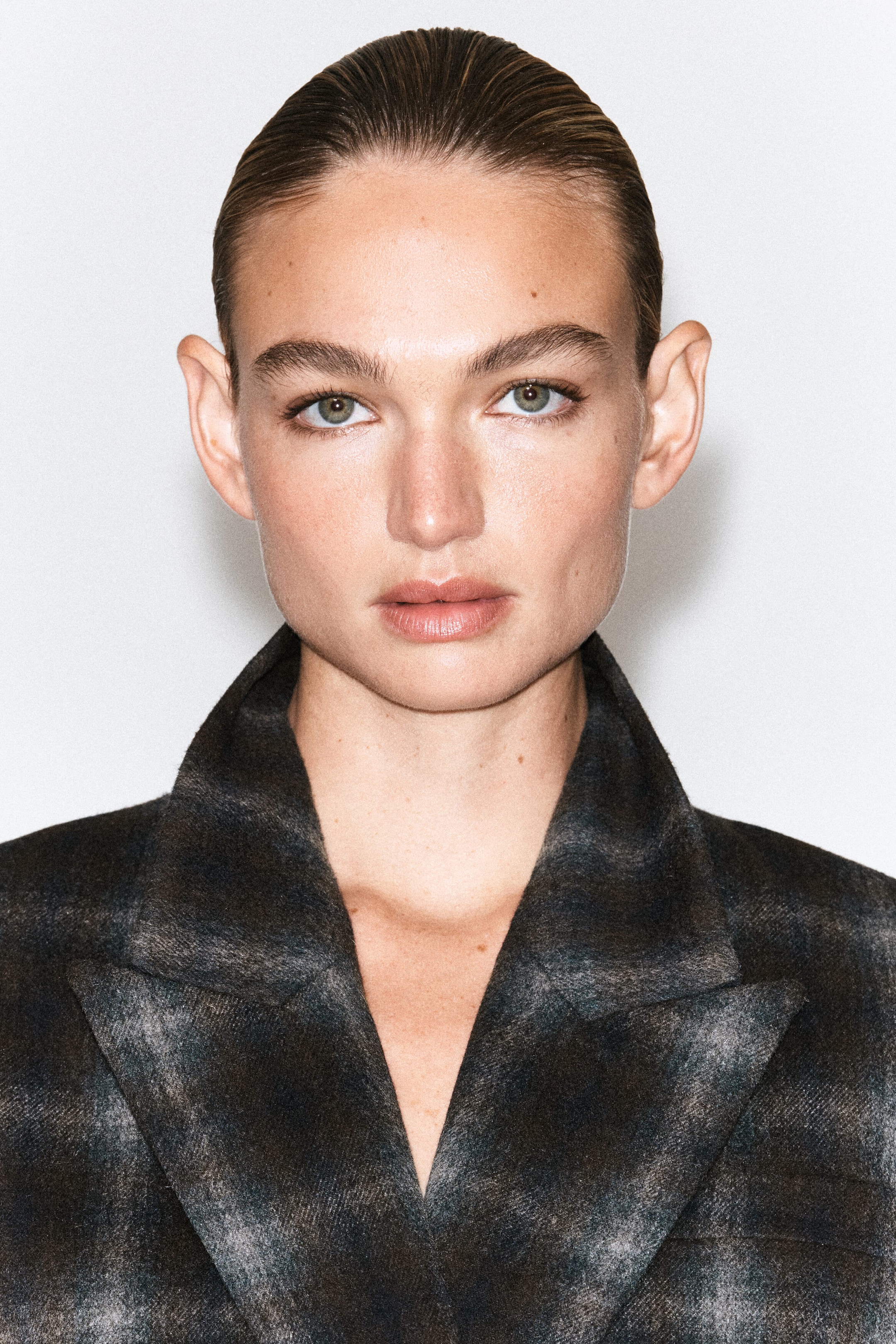 Un blazer en mélange de laine à carreaux, dans un motif tartan foncé, est porté par le mannequin, mettant en valeur son col structuré et ses larges revers en pointe.